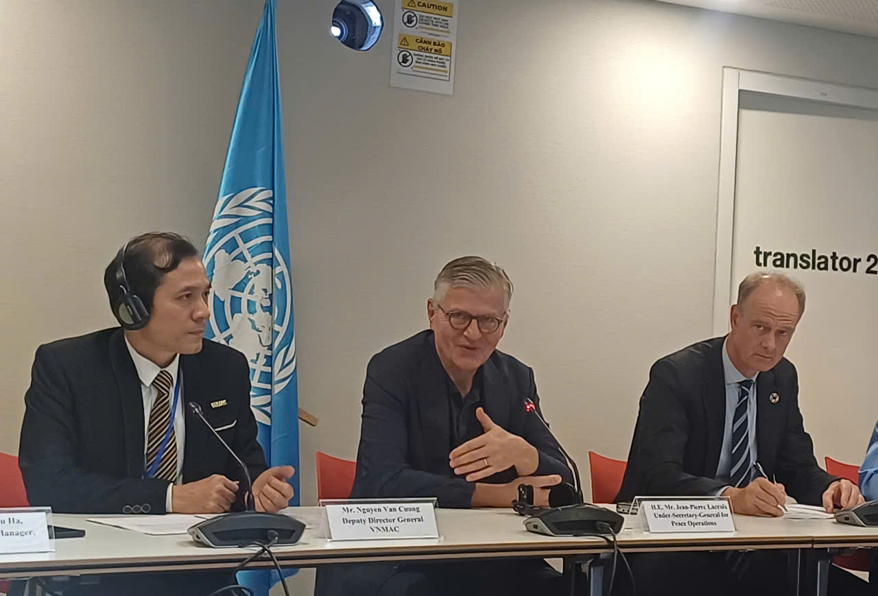 Three men seated at a table with a UN flag in the background, discussing an agenda.