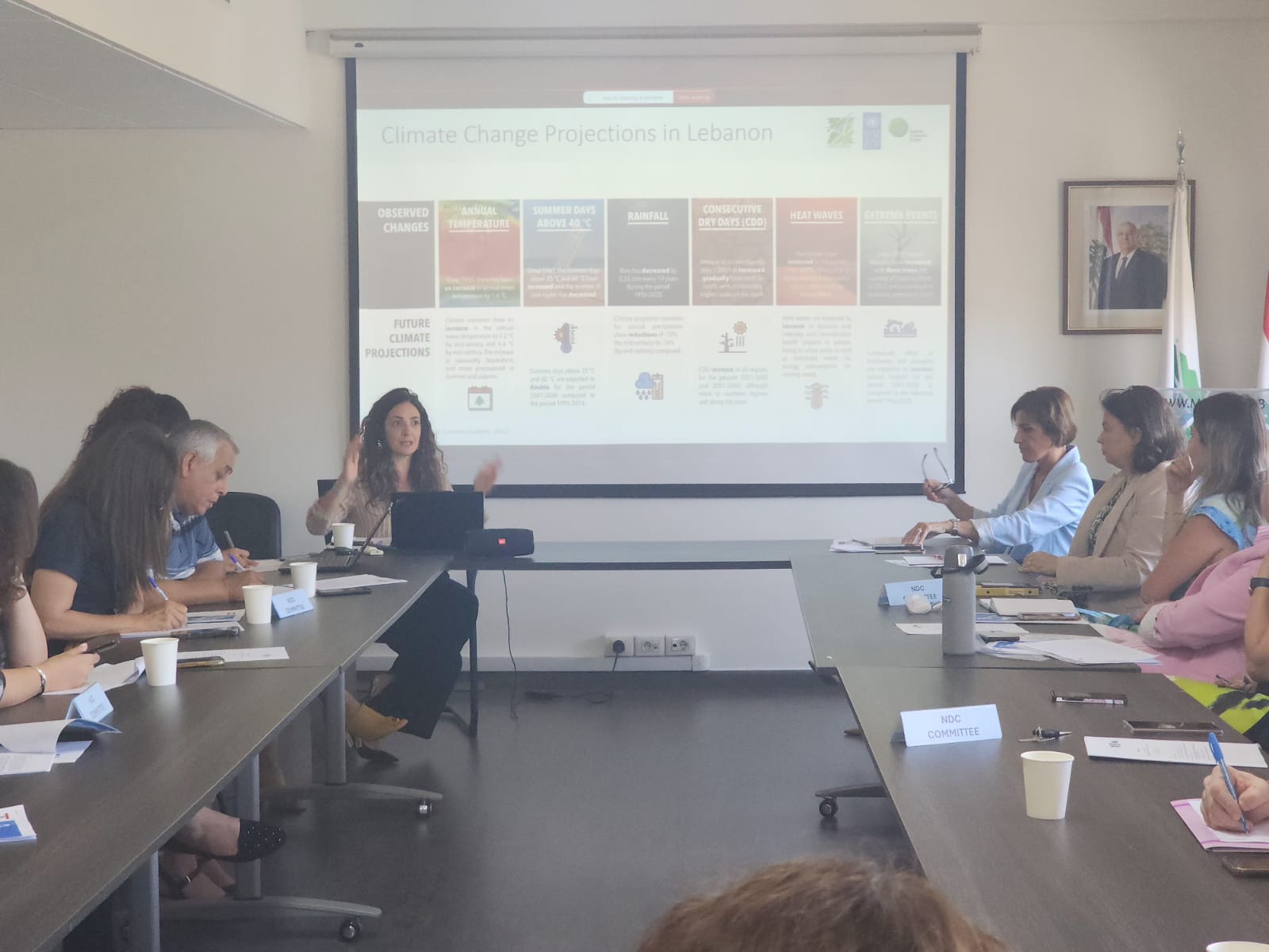 A woman presents at a conference table with colleagues, discussing climate change programs.