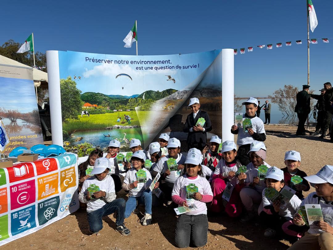Group of children in white caps holding pamphlets, posing in front of a colorful banner.