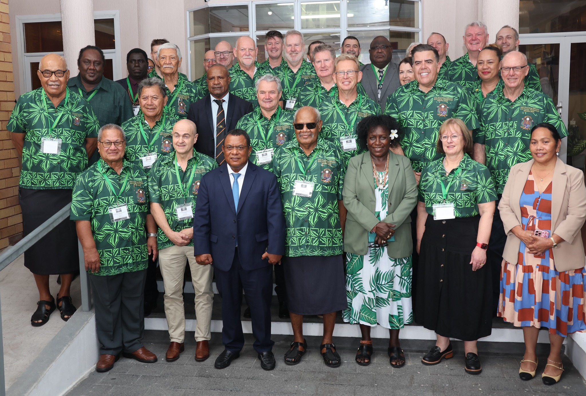 Group photo of attendees in green patterned shirts, smiling in a conference setting.