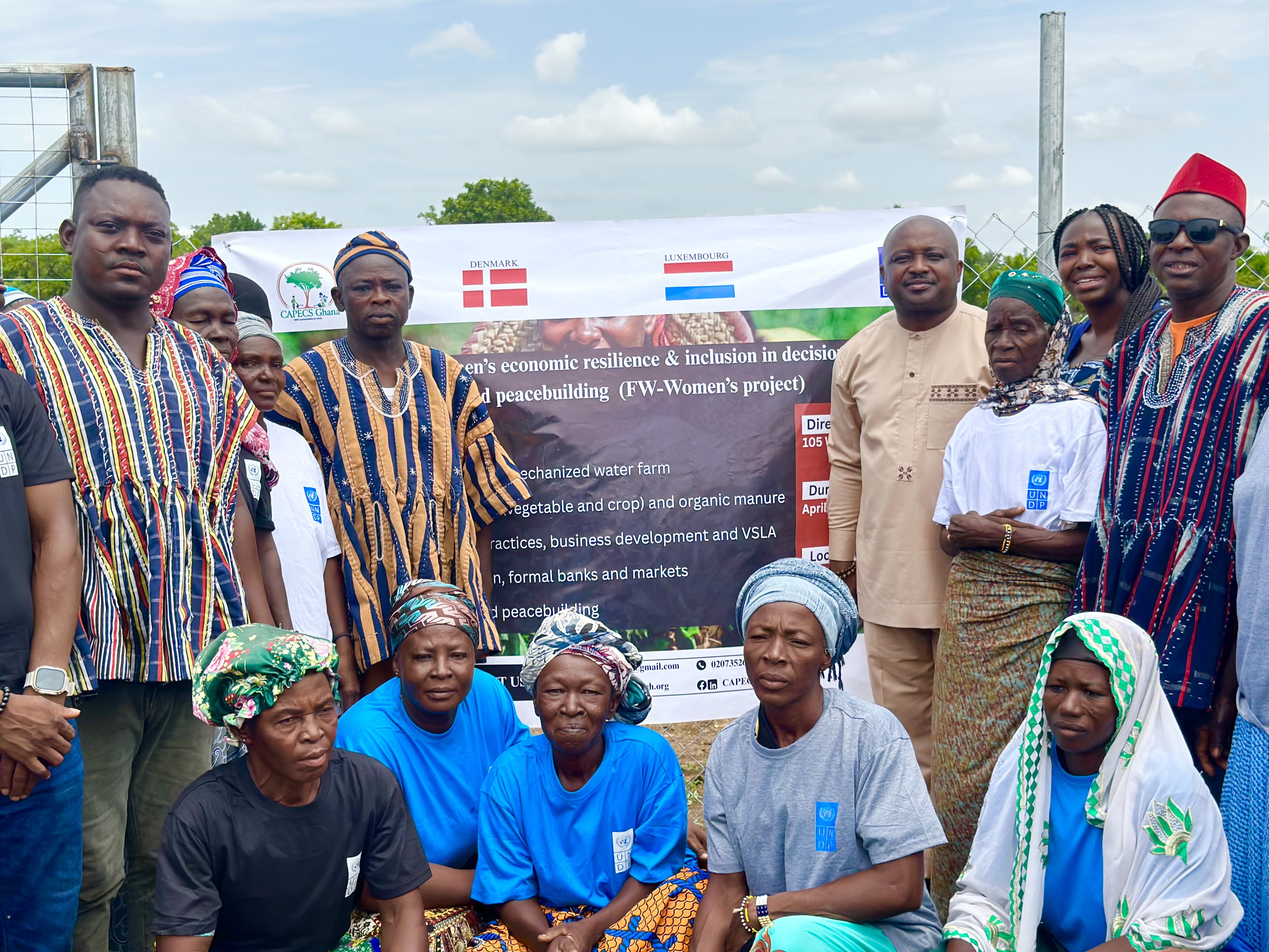 A group of people in traditional attire posing in front of a banner outdoors.