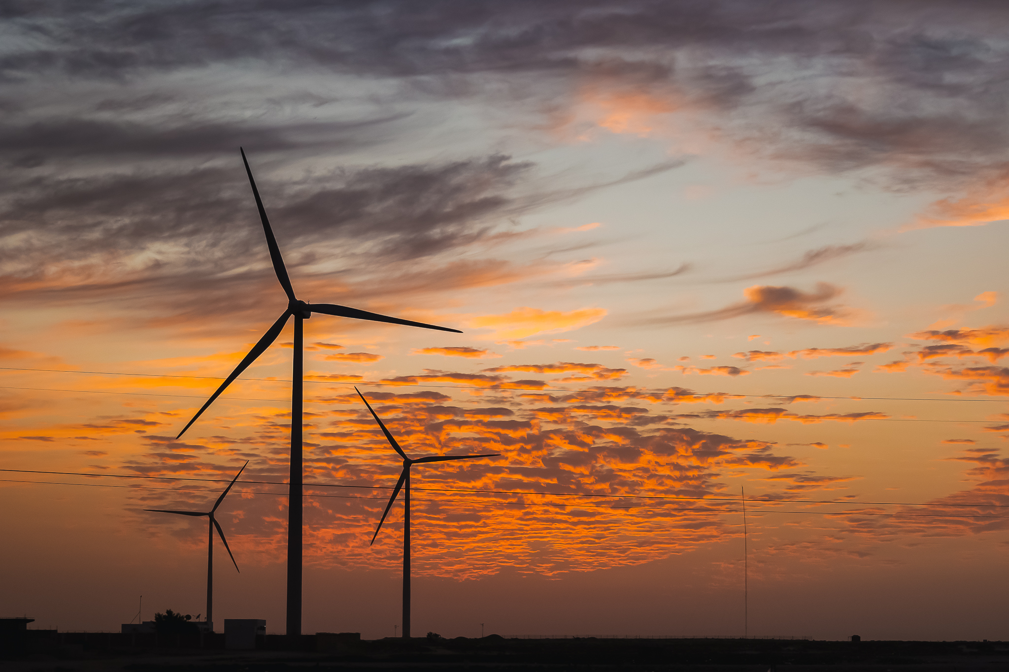 Silhouettes of wind turbines against a vibrant sunset sky with orange and purple hues.