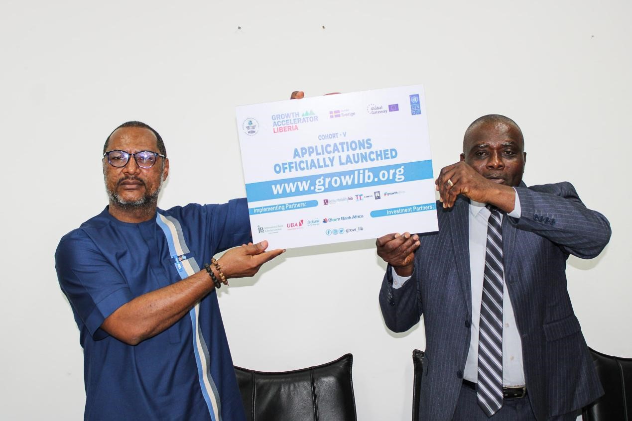 Two men hold up a sign announcing the launch of applications, smiling.