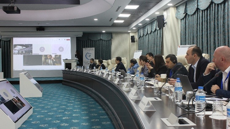 Business meeting around a conference table with participants engaged and a presentation displayed.