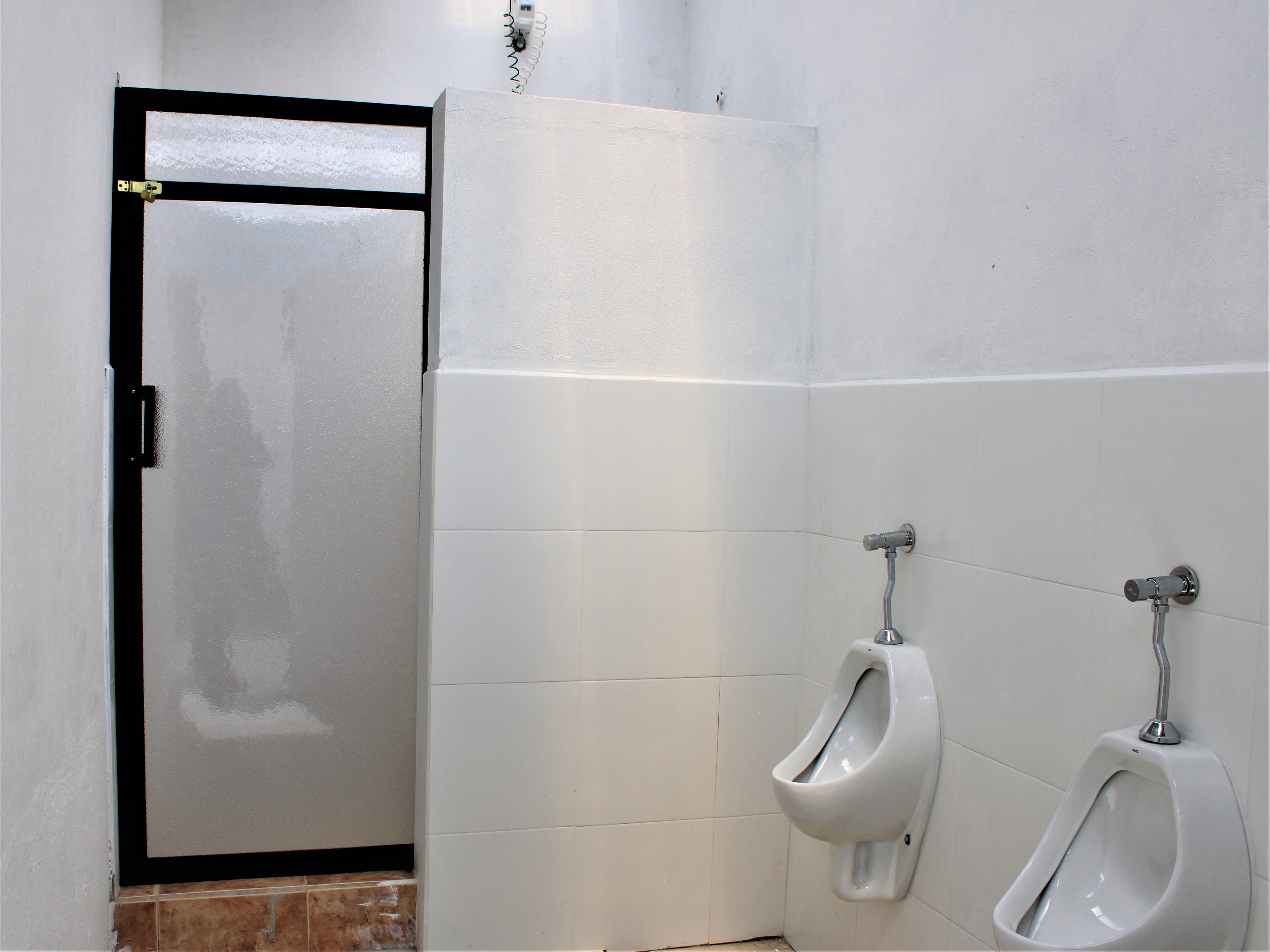 Men's restroom with two white urinals and a partially visible door. Walls are clean and tiled.