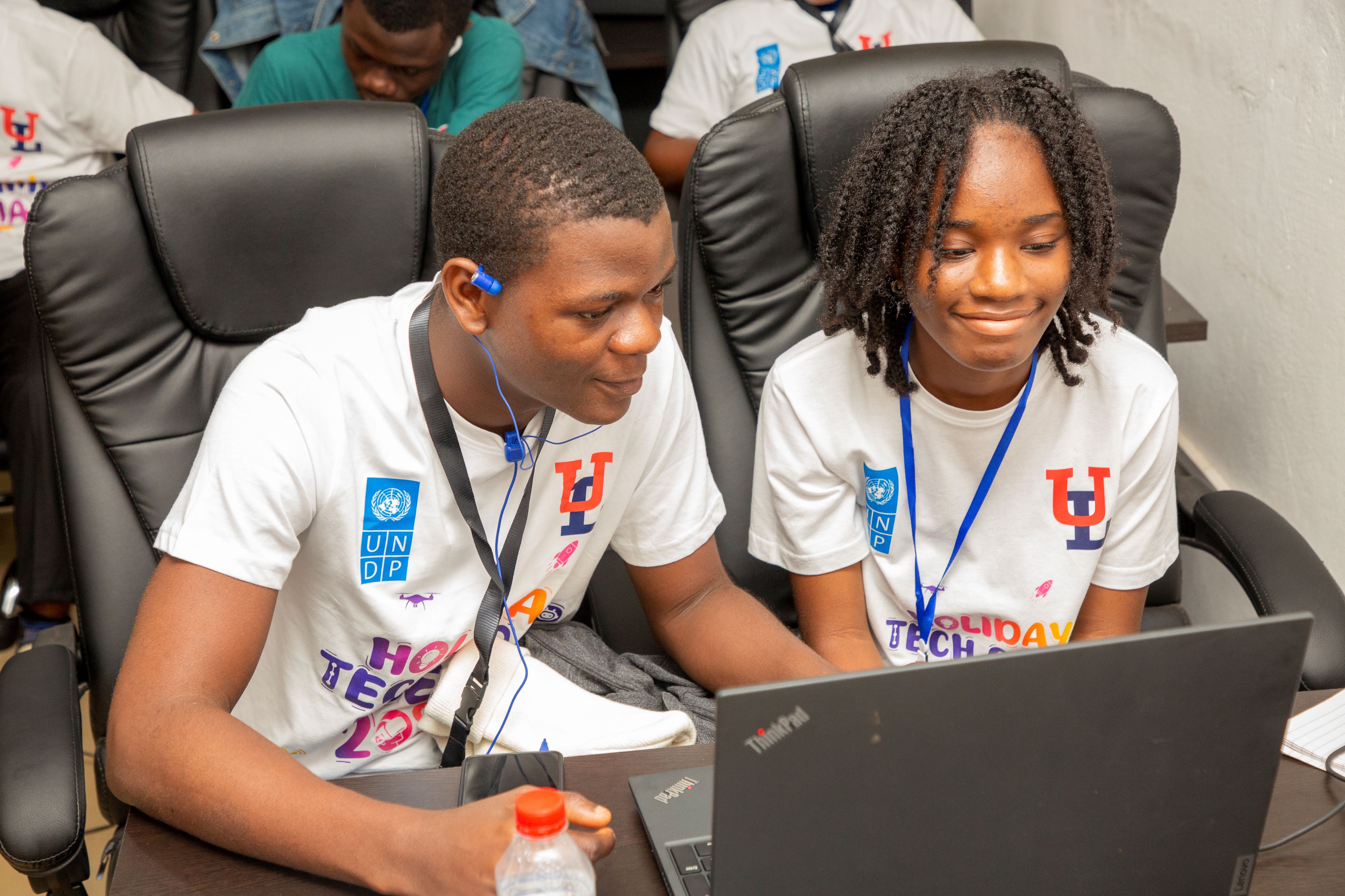 Two young individuals collaborate on a laptop, both wearing matching t-shirts and focused.