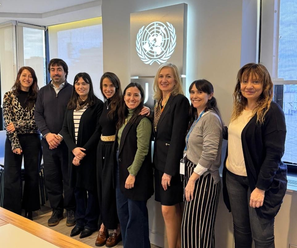 Un grupo de nueve personas sonriendo juntas en una oficina, con el logo de PNUD en el fondo.