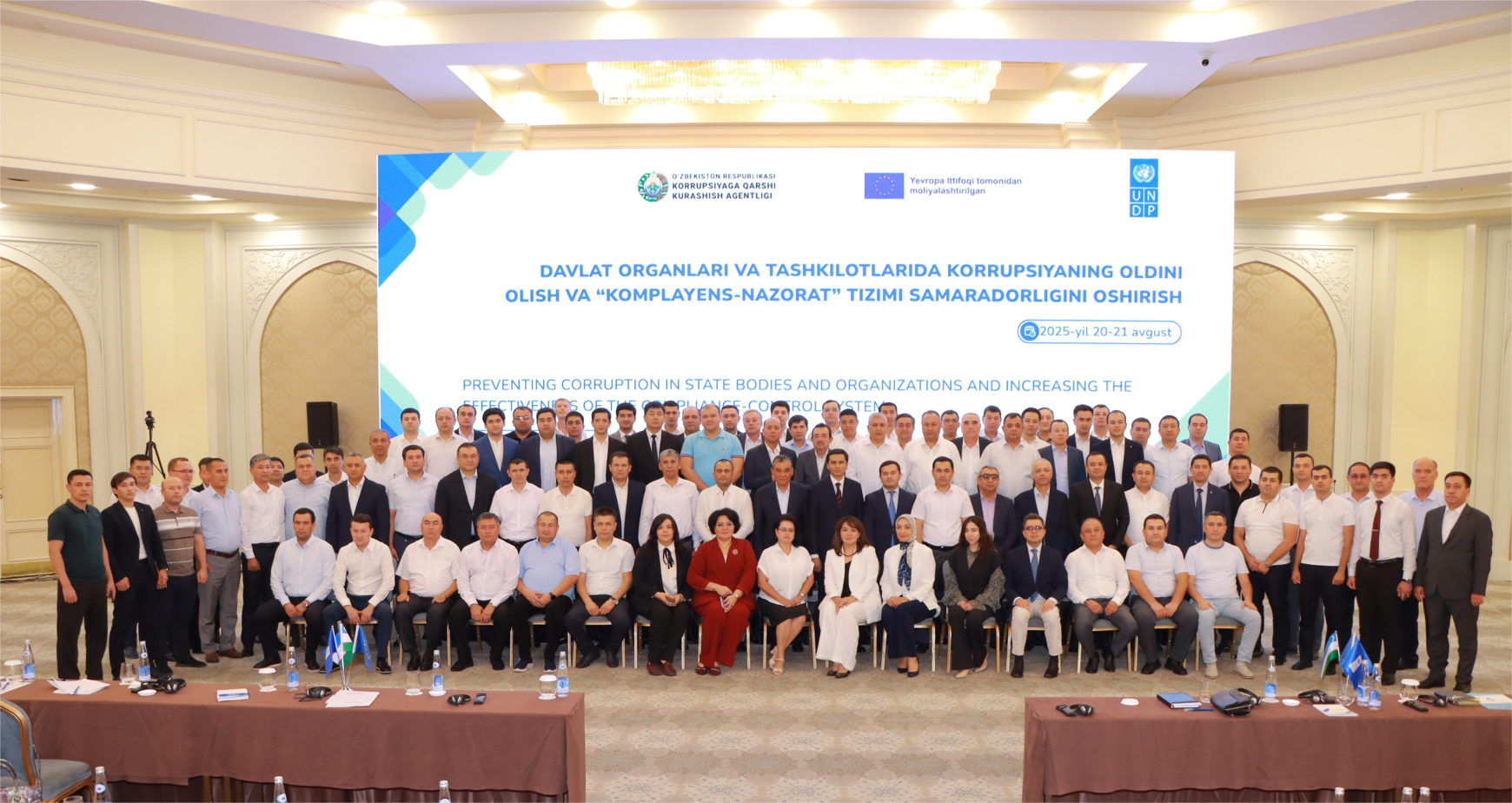 A large group of people posing together in a conference hall, smiling at the camera.