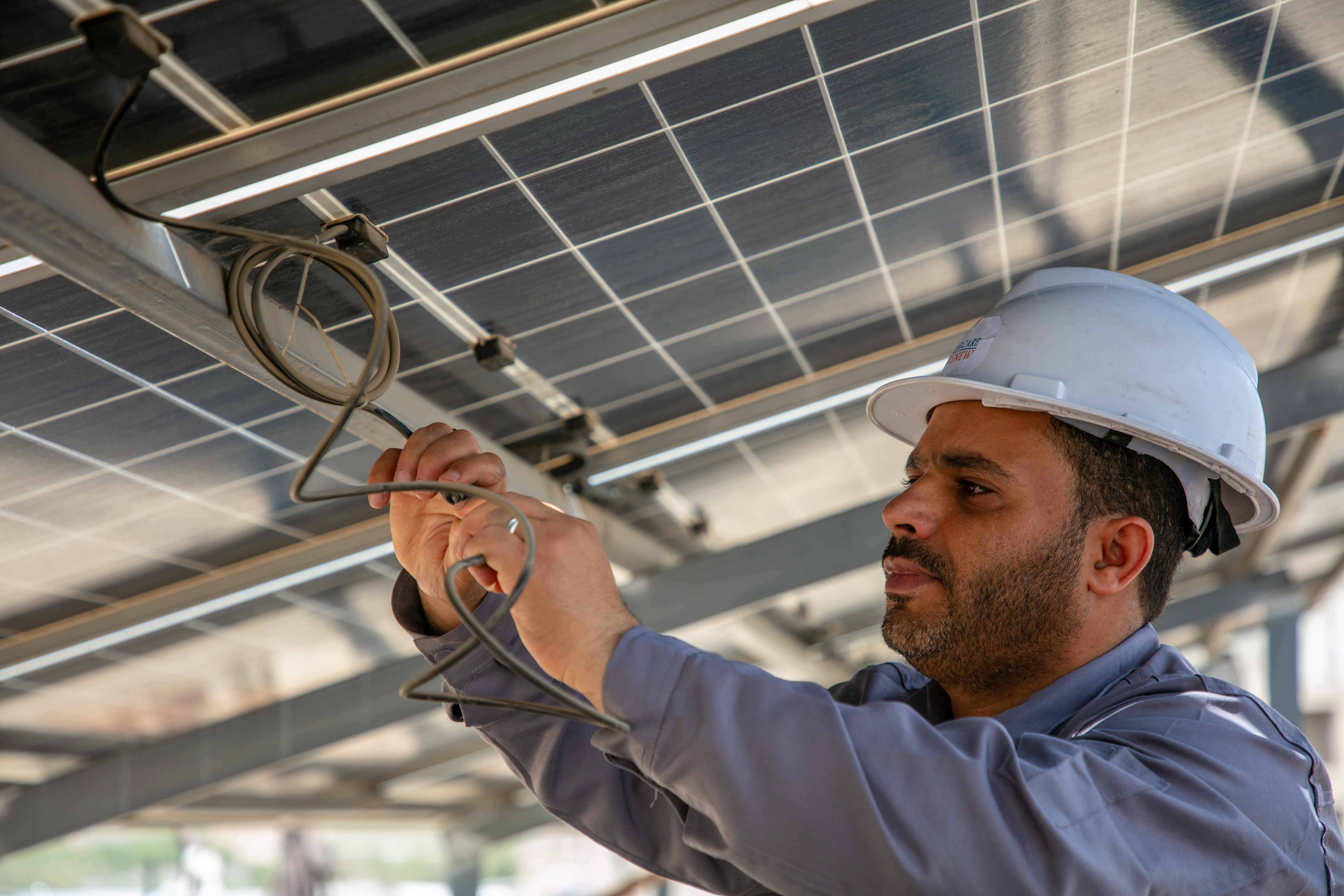 A worker in a hard hat connects wires under solar panels.