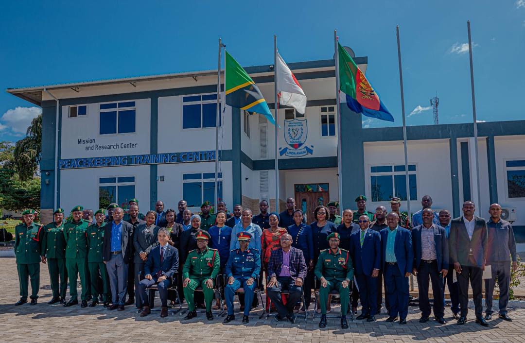 Group photo of people in military uniforms and formal attire outside a building with flags.