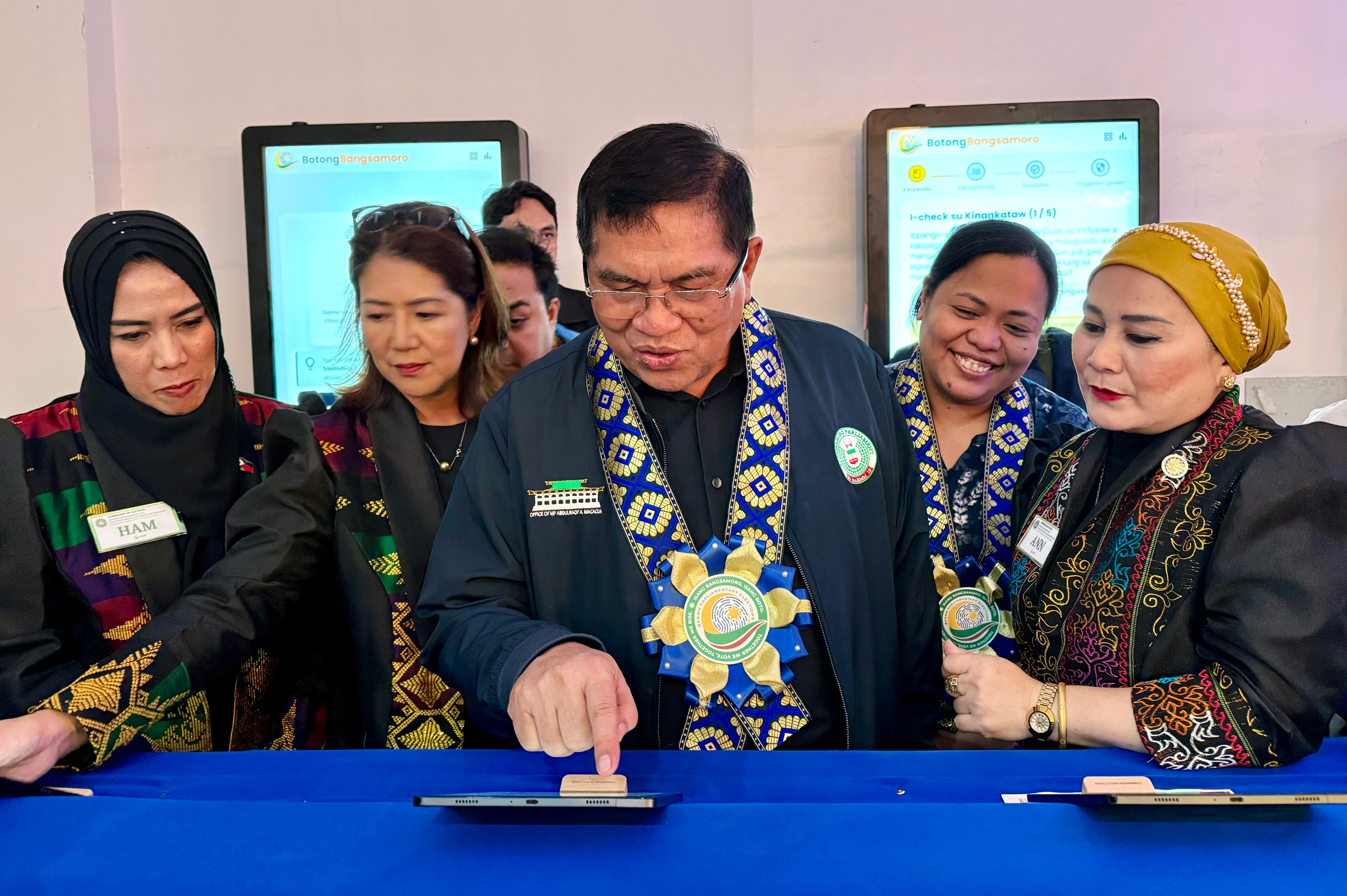 A group of people in traditional attire interacting with a touchscreen device.
