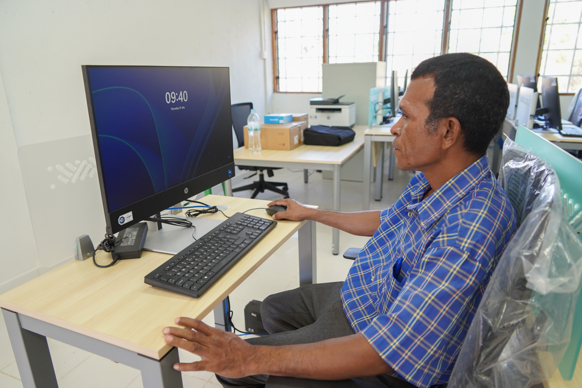 Man sitting at a computer desk, working on a desktop monitor in a bright room.