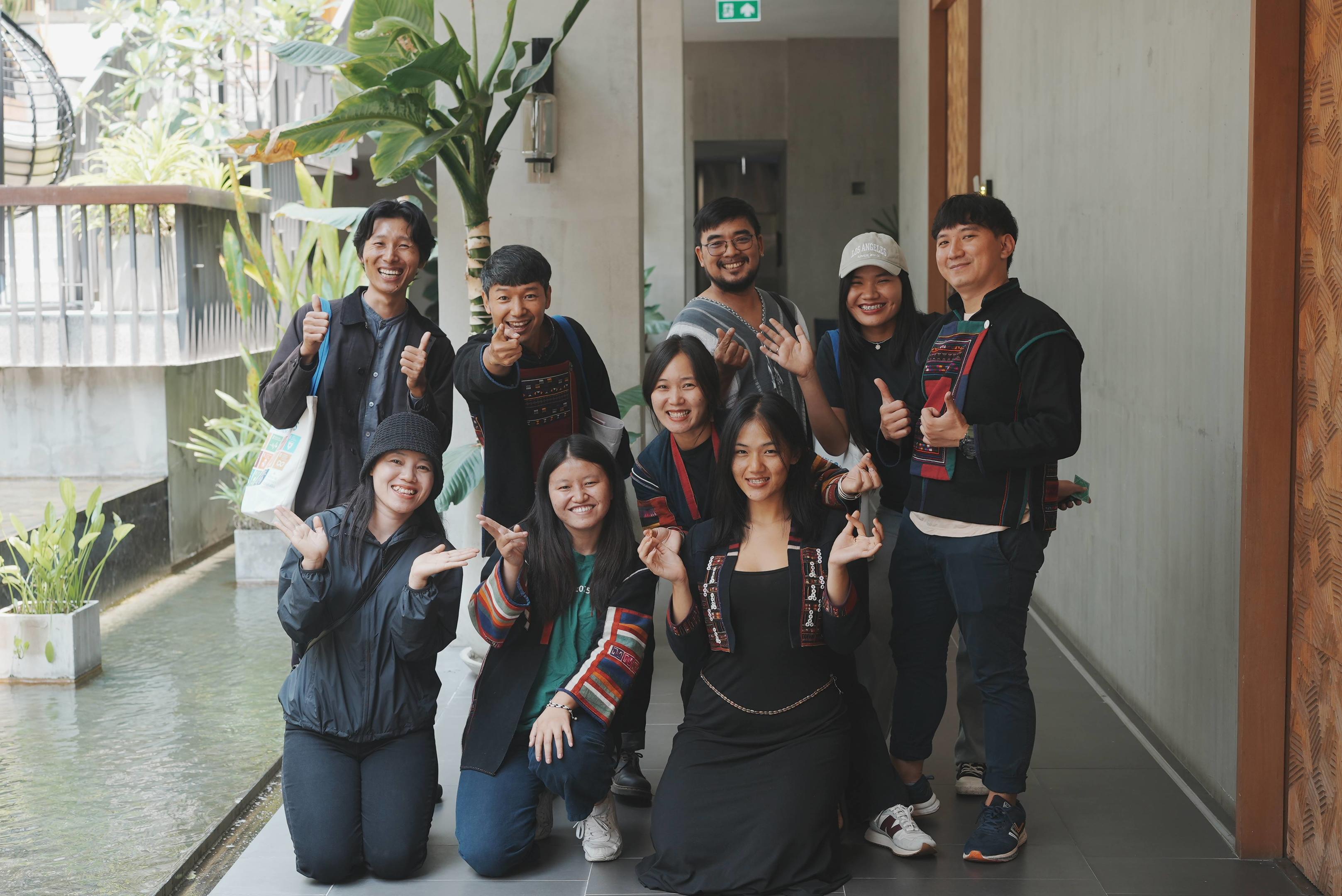 A group of smiling people posing together in a hallway with plants nearby.