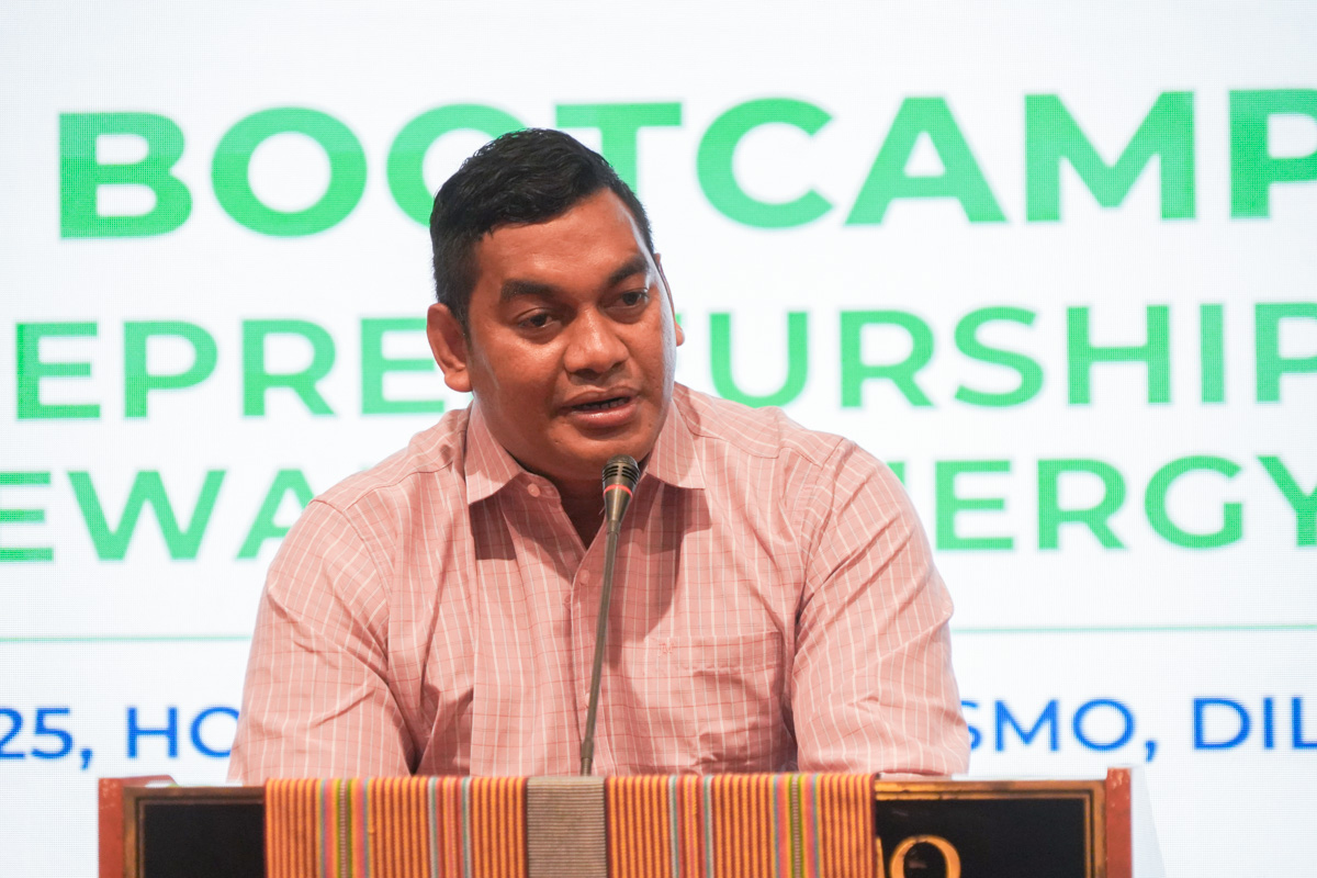 A man in a pink shirt speaks at a podium during an entrepreneurship bootcamp event.