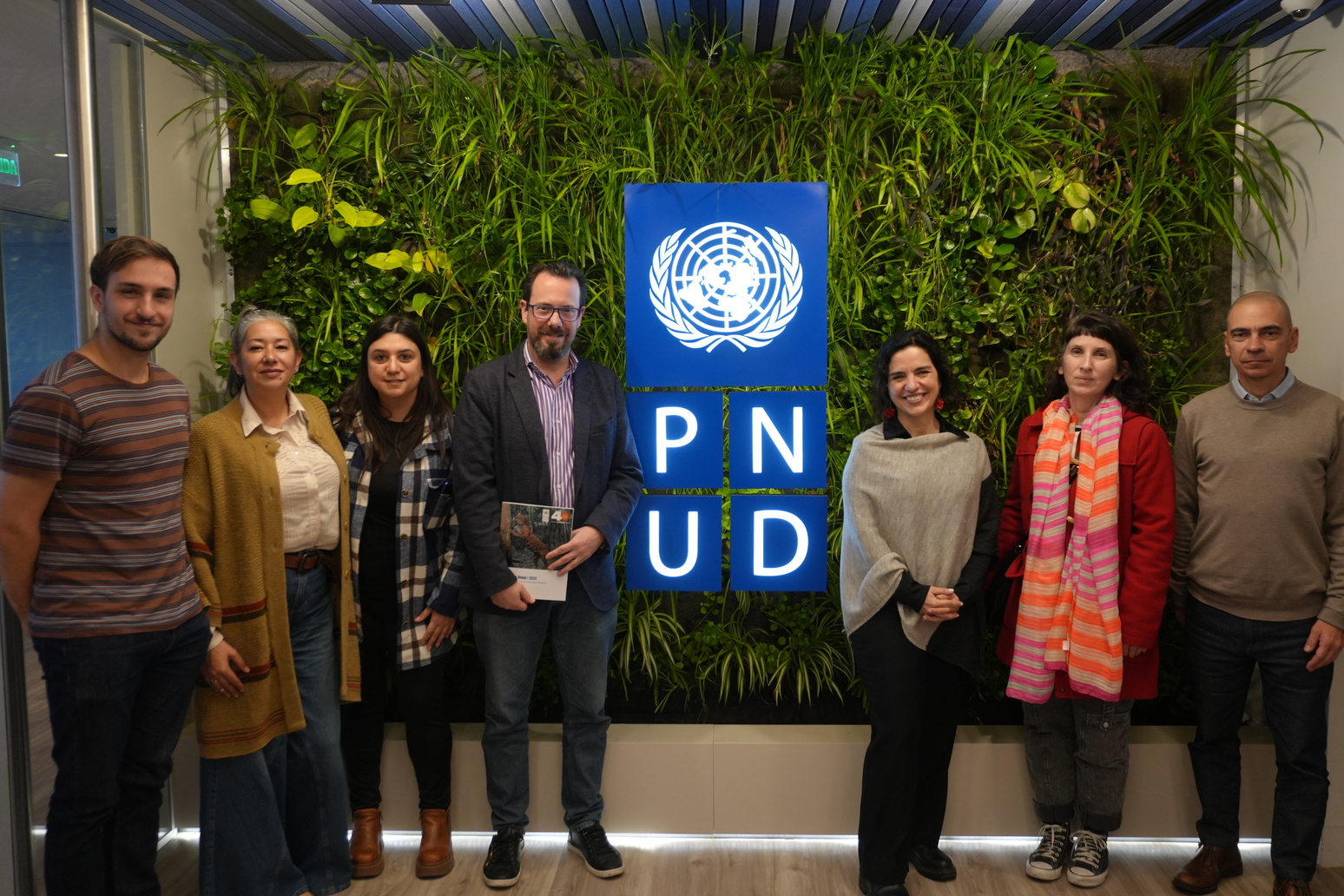 Group of six people standing in front of a green wall with the PNUD logo.