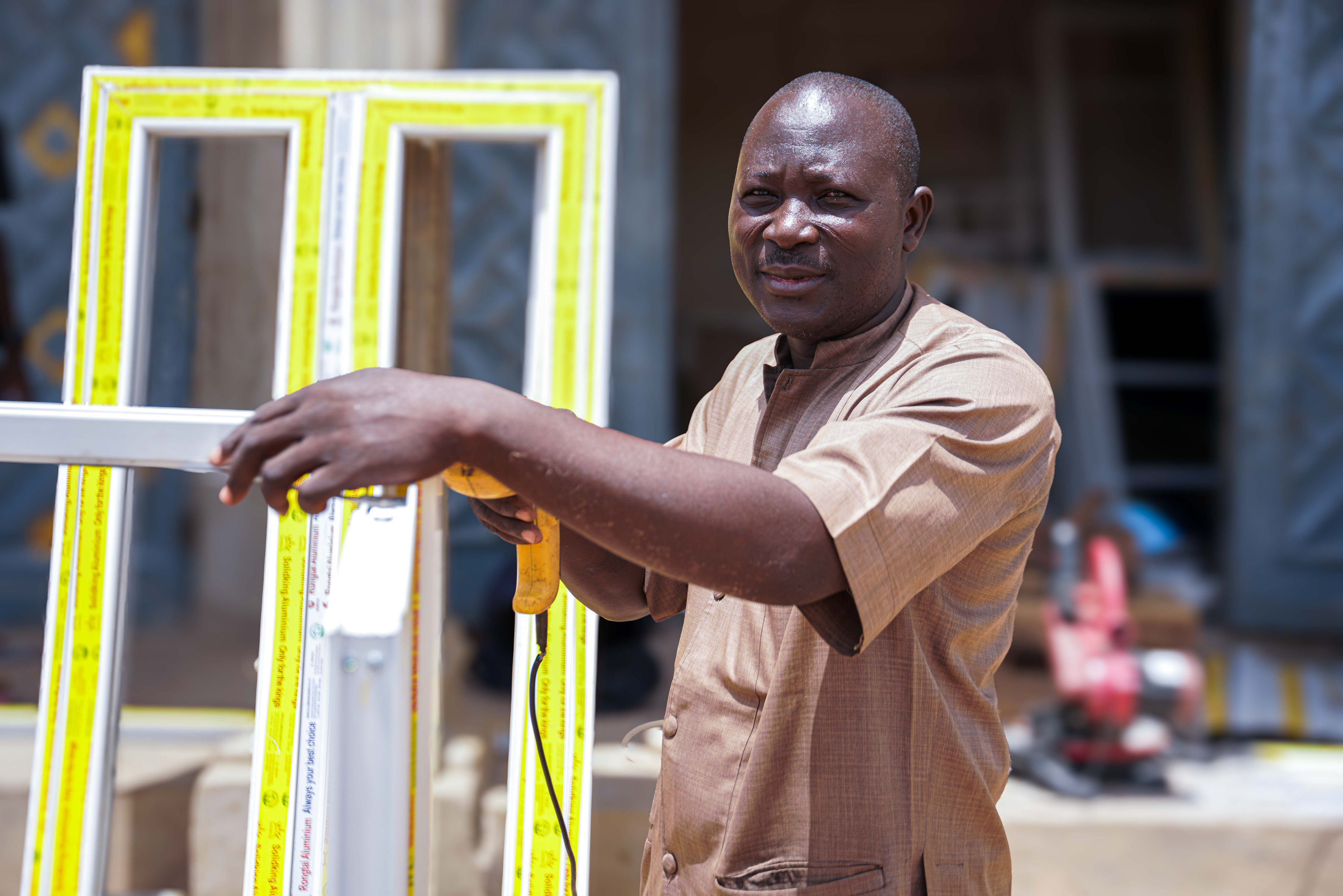 A man holds a measuring tool near a window frame, focused and working outdoors.