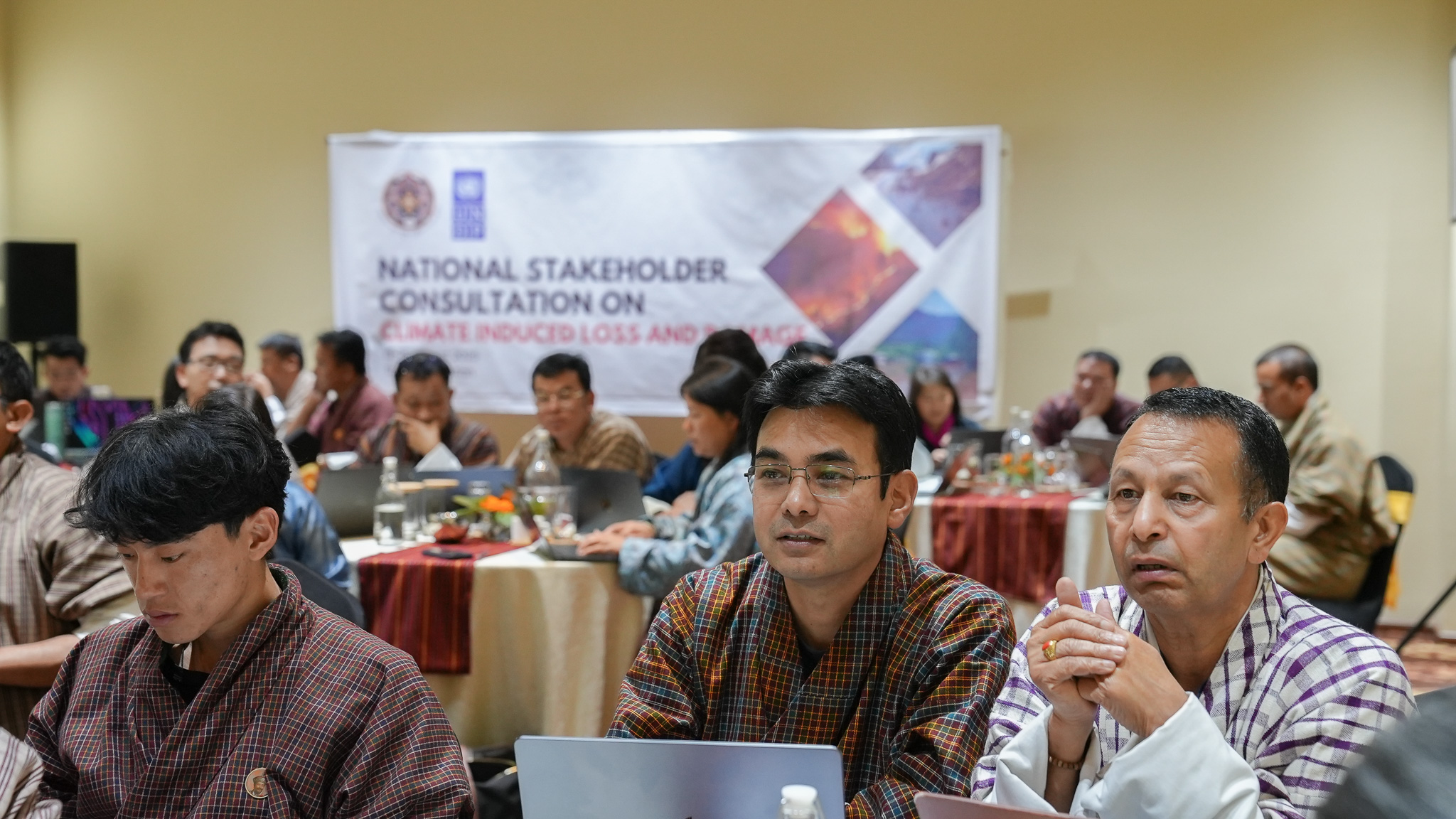 Group of people engaged in a meeting, with laptops and a banner in the background.