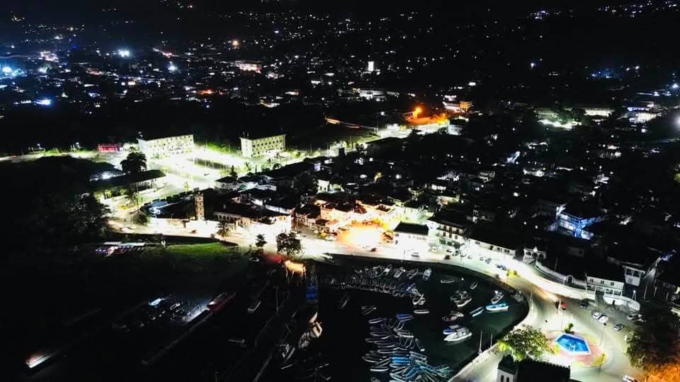 Night aerial view of a vibrant town, illuminated streets, and a marina.