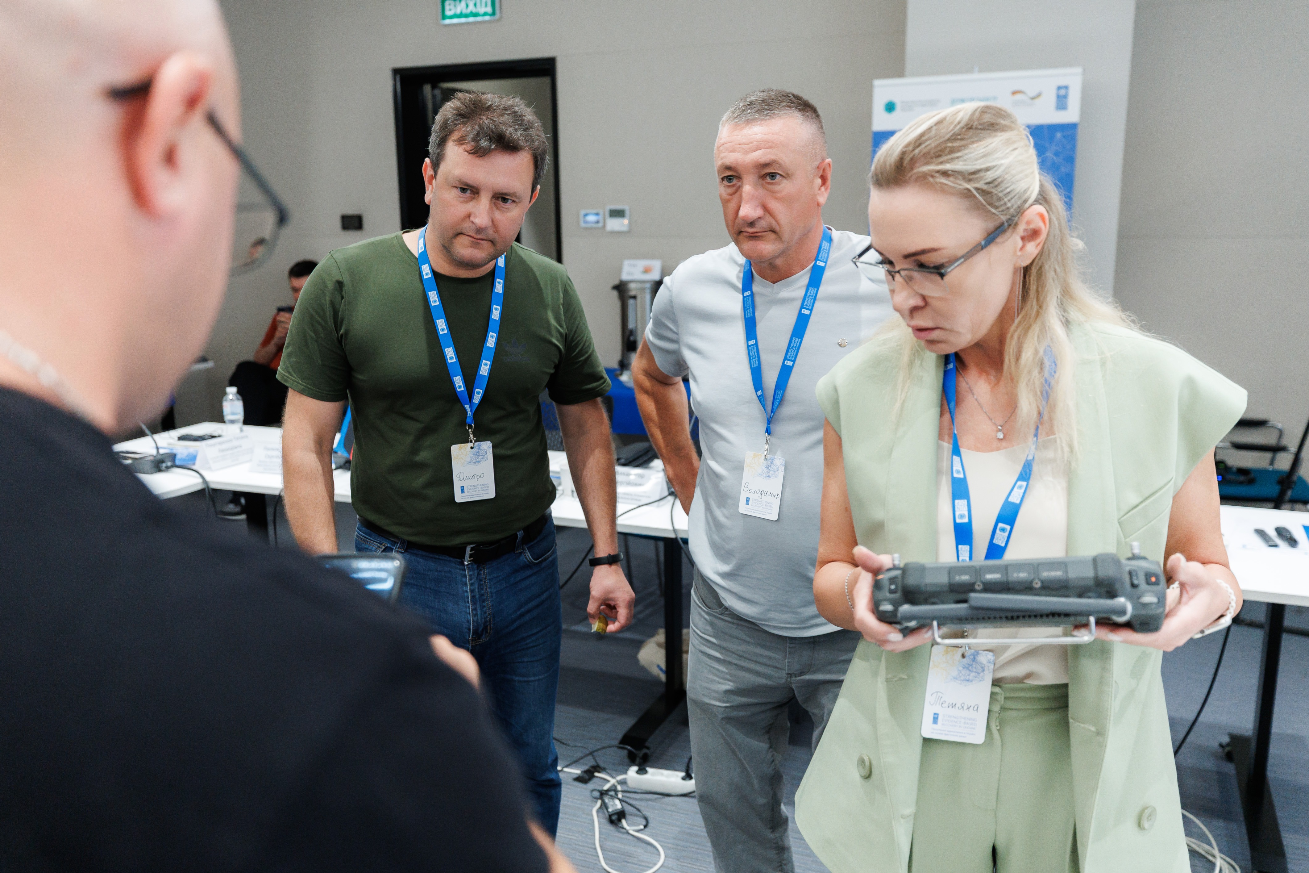 Four individuals engage in a discussion, examining a device in a conference setting.