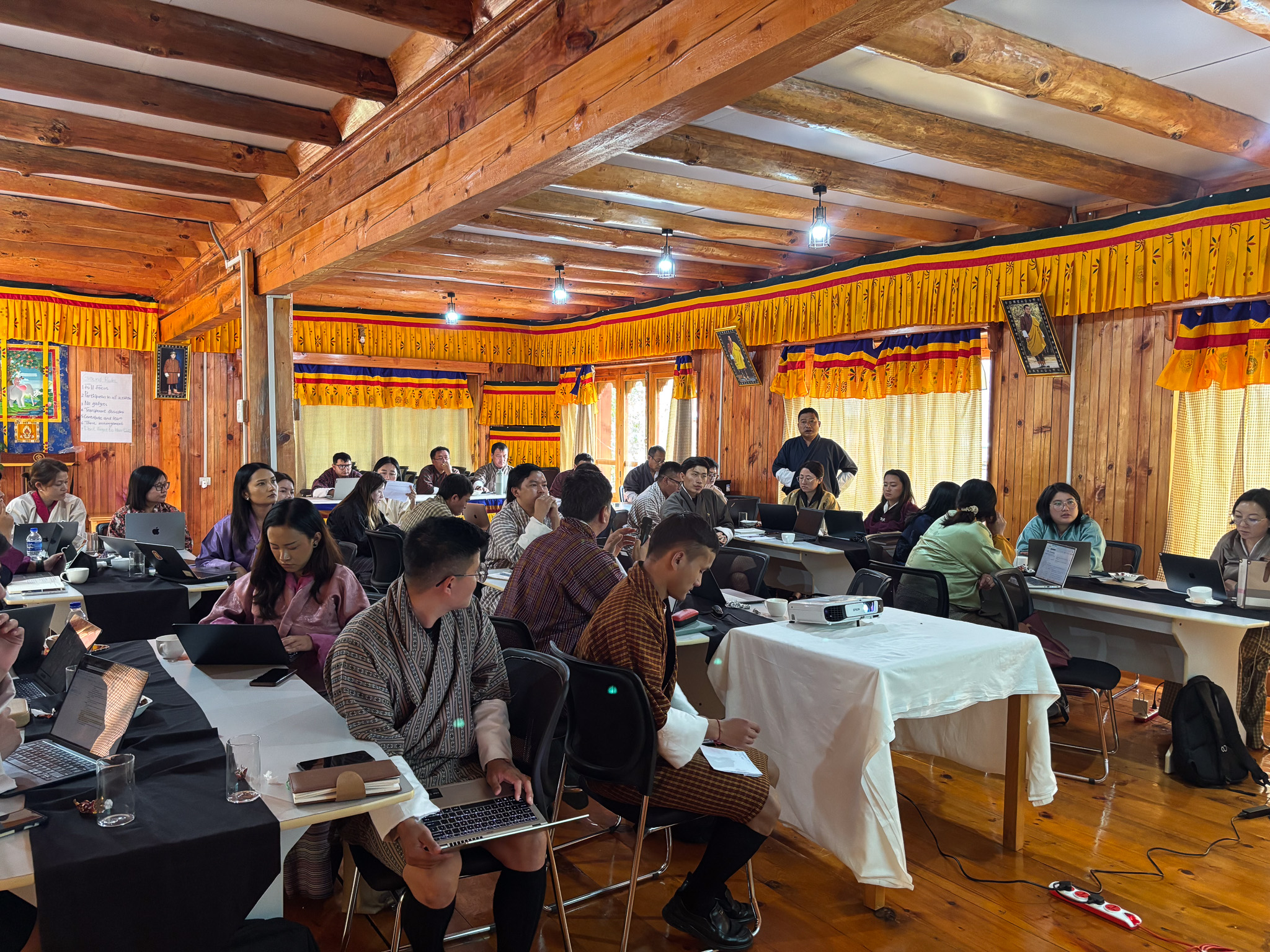 A group of people seated at tables in a wooden room, engaged in a seminar or workshop.