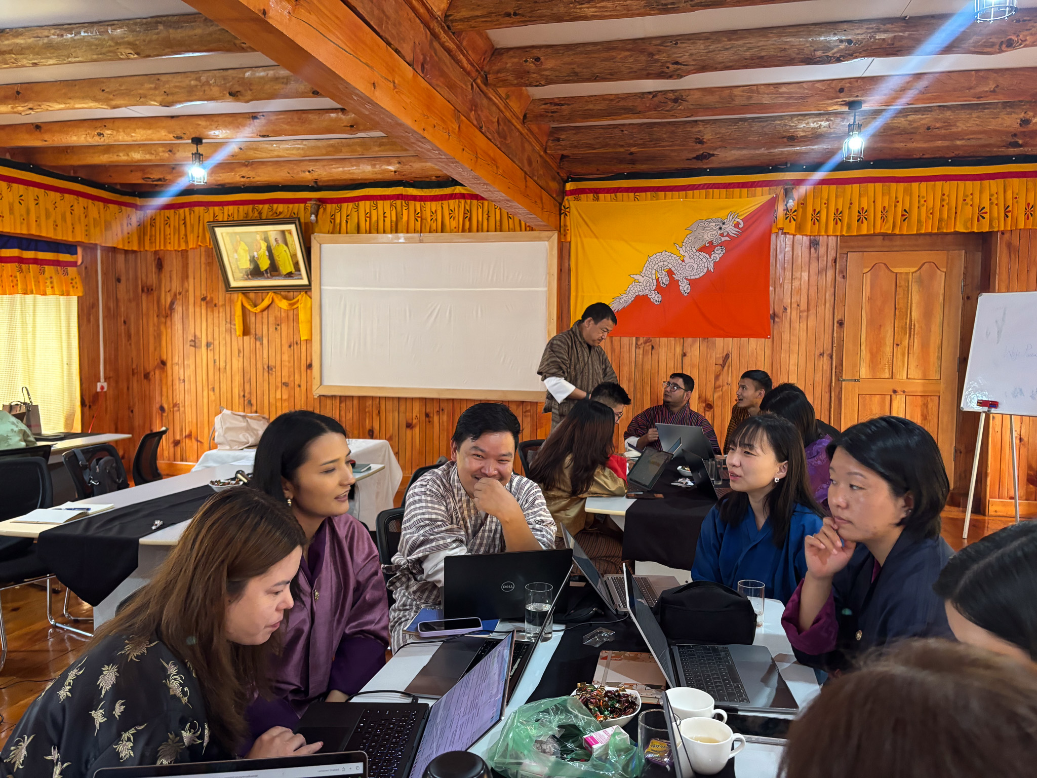 A group of people engaged in discussion around tables in a wooden room.
