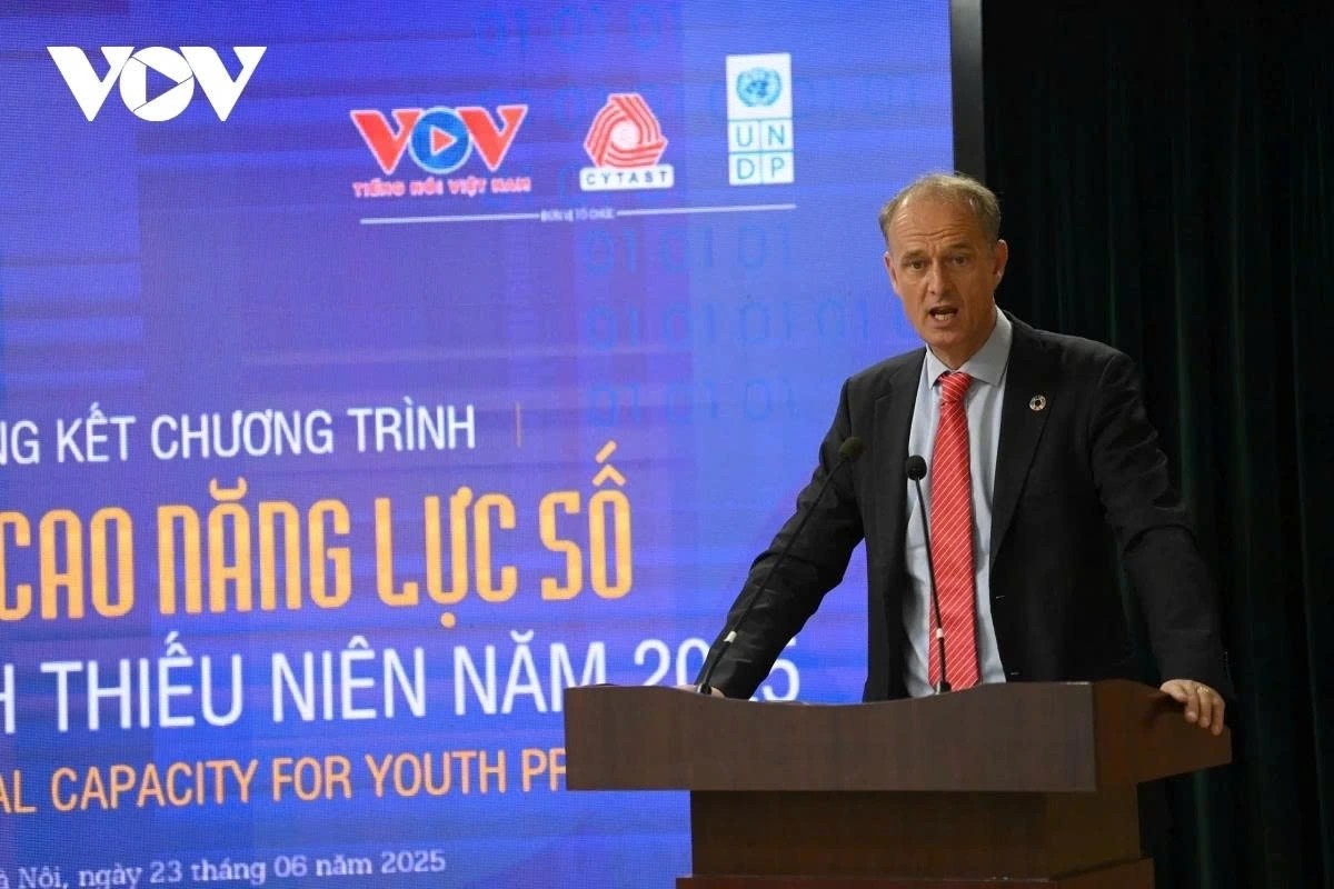 A man in a suit speaks at a podium during a conference, with banners in the background.