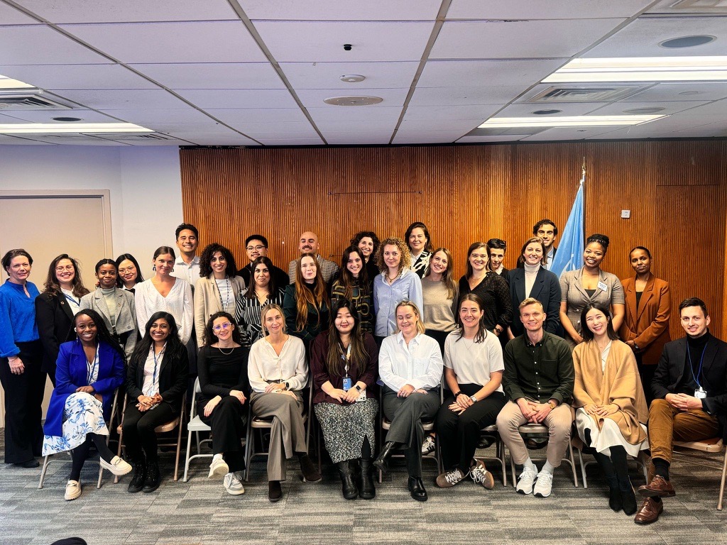 Group photo of diverse individuals posing together in an indoor setting with a wooden backdrop.