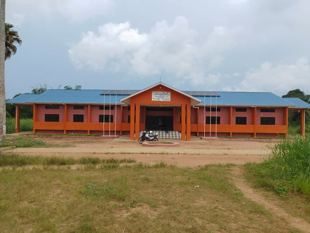 Orange building with a blue roof, surrounded by grass and trees under a cloudy sky.