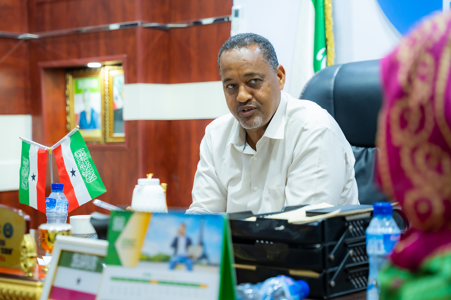 A man in a white shirt sits at a desk, engaged in conversation with a woman.