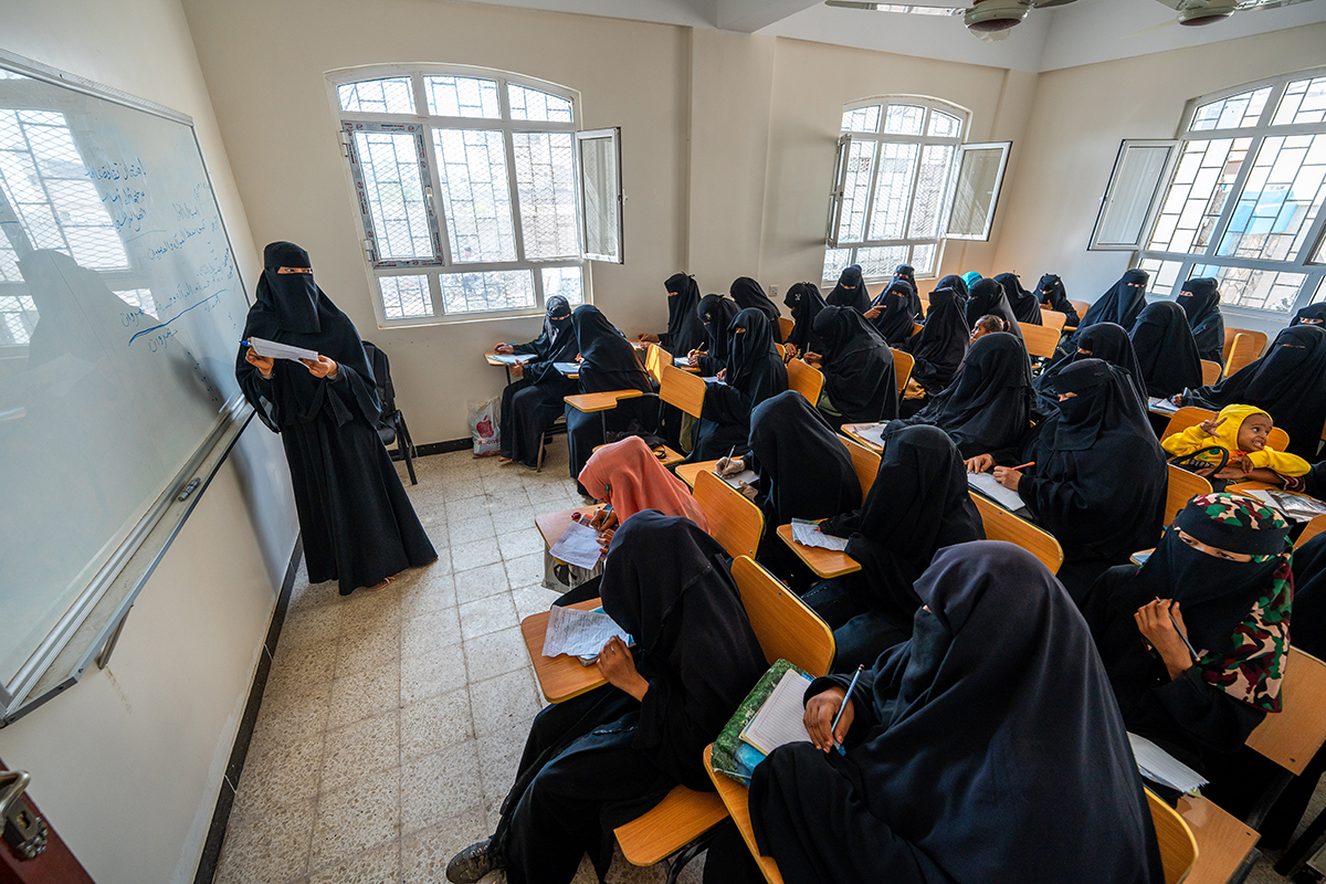 A classroom filled with female students in black attire, attentively listening to a teacher.