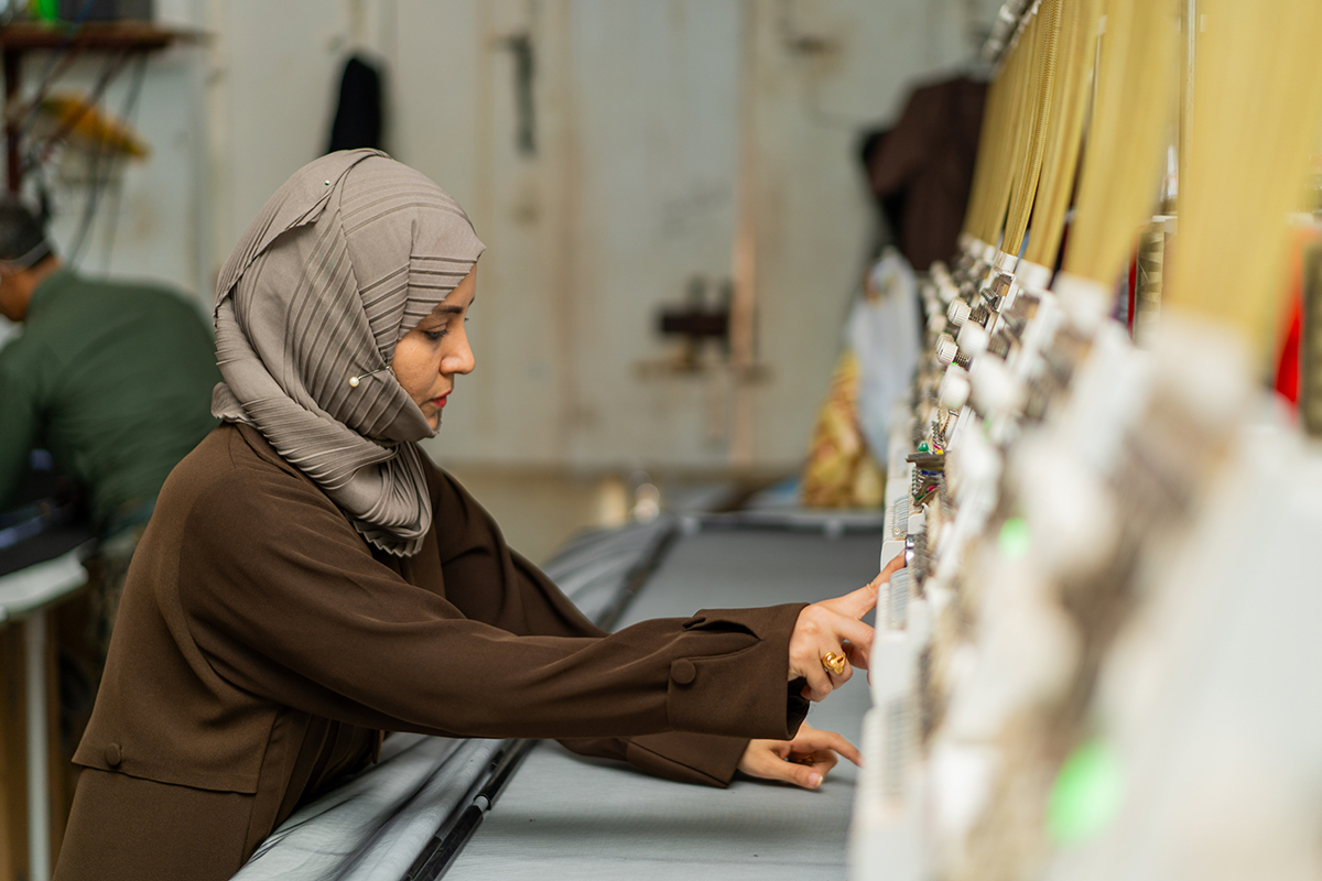 A woman in a hijab focuses on an equipment in a well-lit workshop.