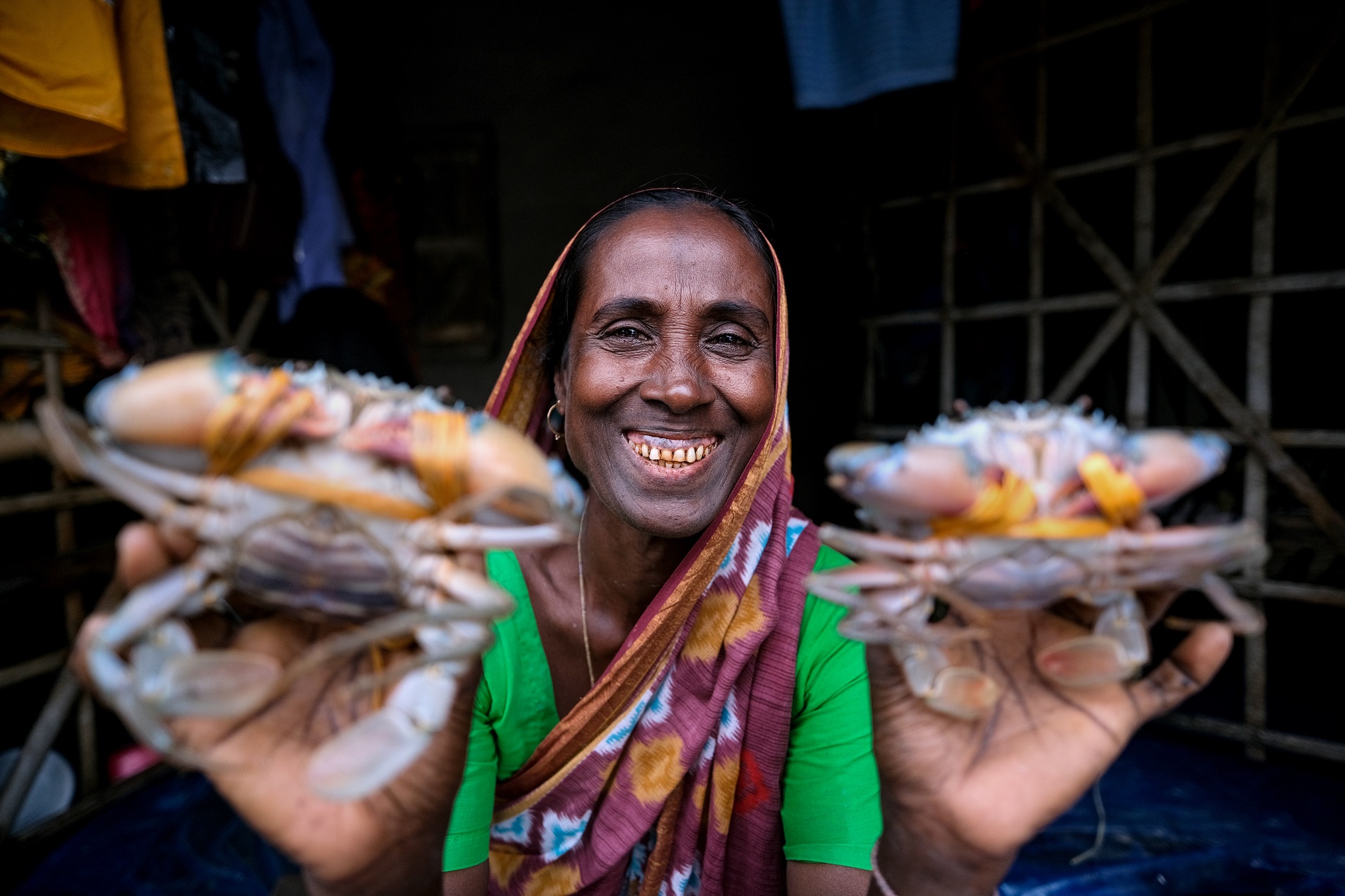Woman smiling and holding two live crabs, wearing a colorful sari, in a market setting.