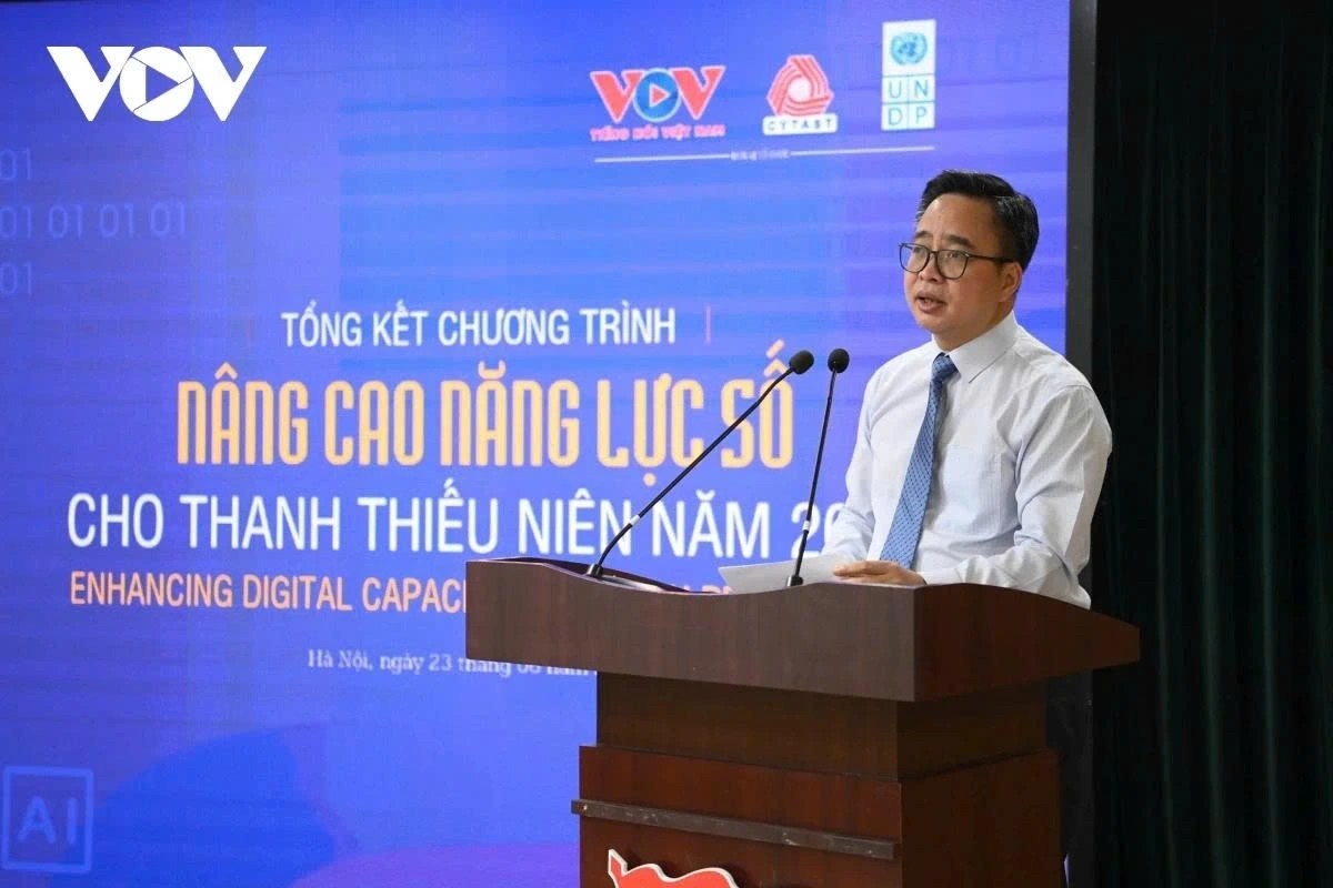 A man in a suit speaks at a podium in front of a blue banner about enhancing digital skills.