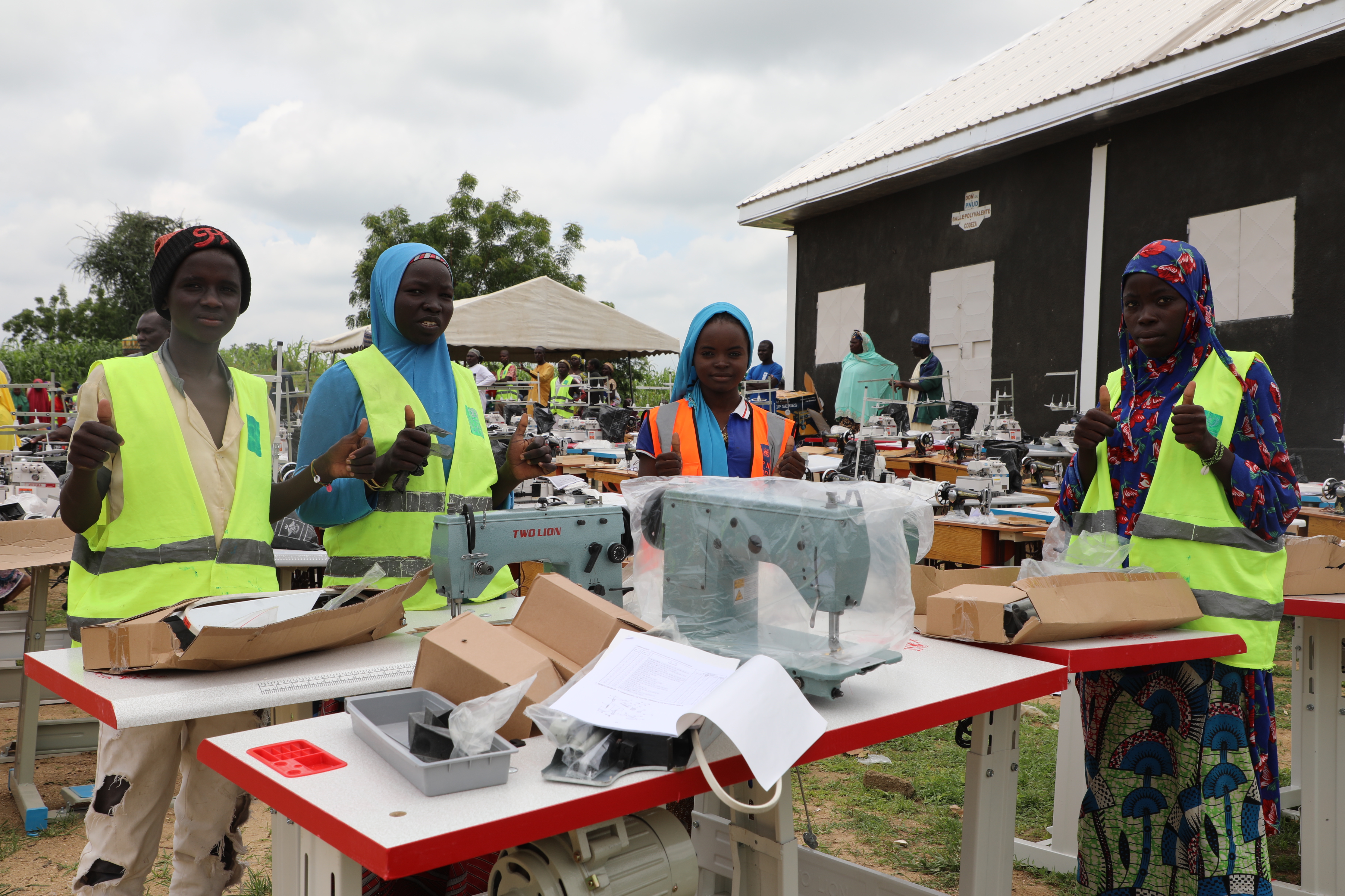 Photograph: group of people in safety vests at a sewing workshop with machines outdoors.