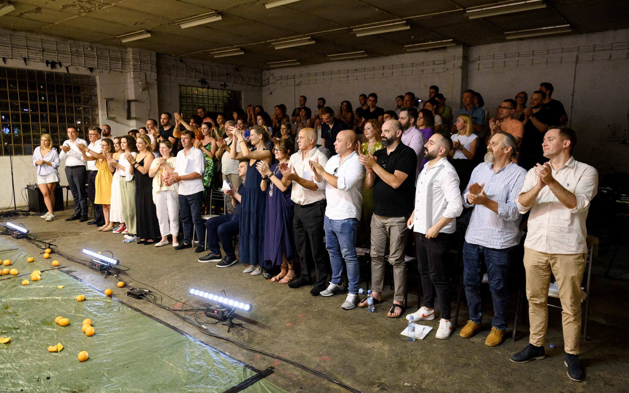 Group of people standing and clapping in a warehouse-like room beside a pool table.