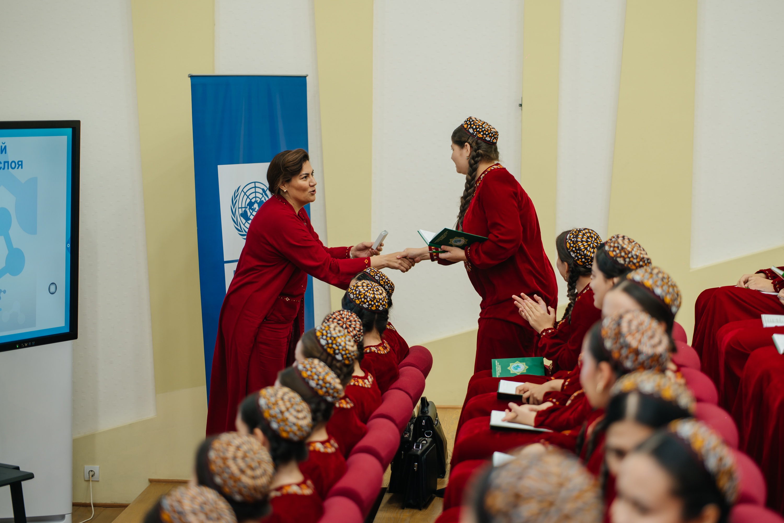 Photograph of red-robed monks seated in rows during a ceremony; two monks greet at front.