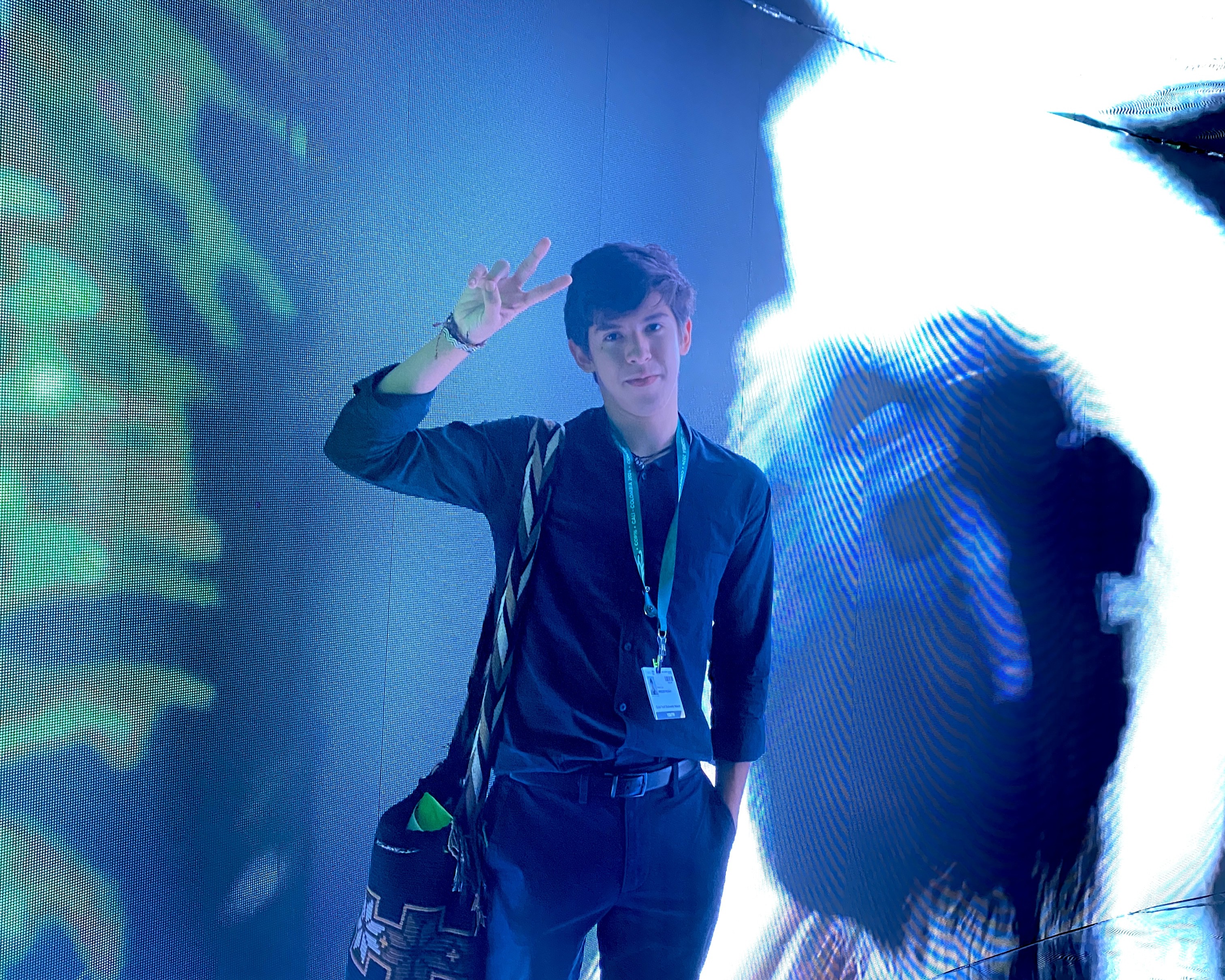 Man in blue outfit with lanyard waving at a conference under blue stage lights.