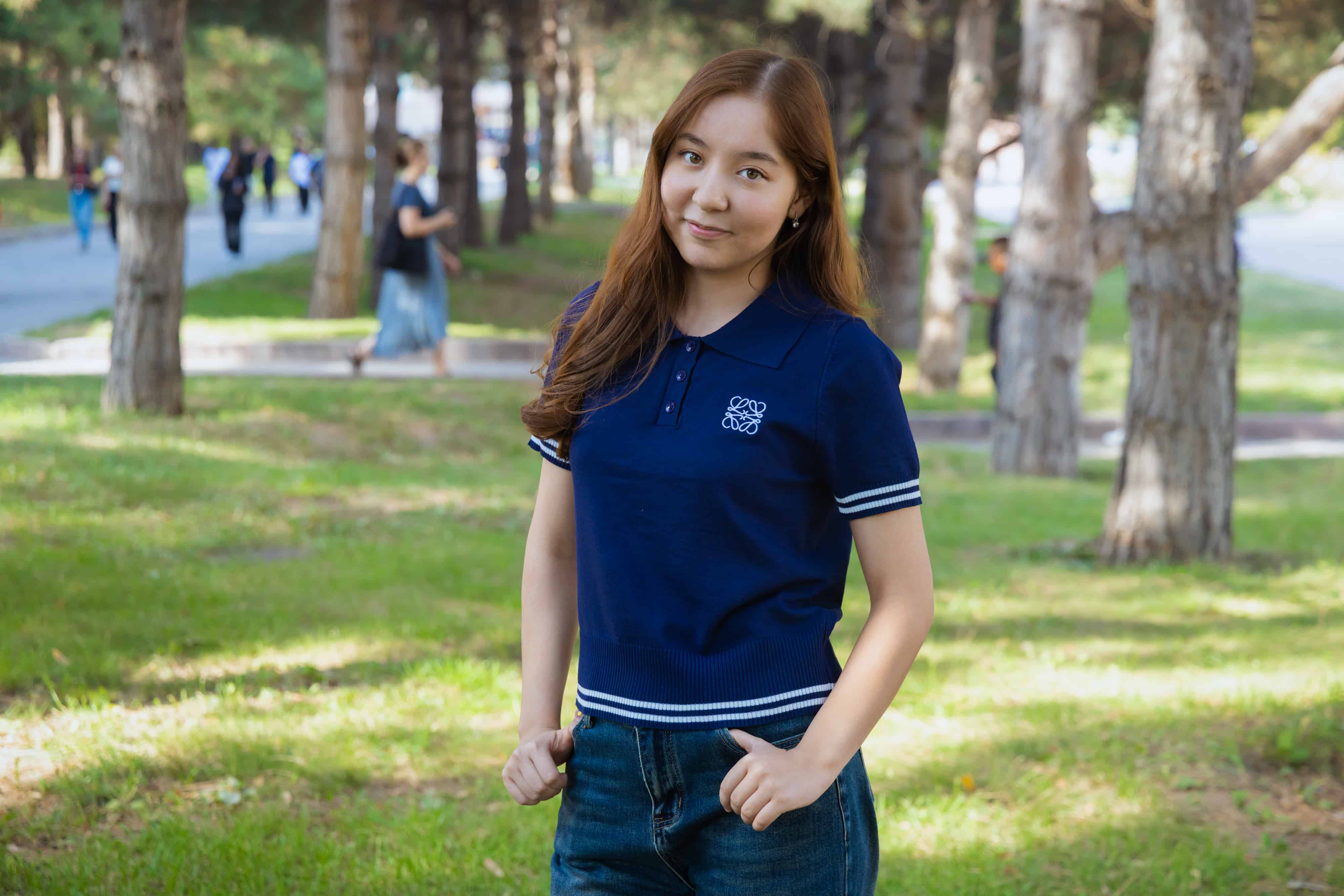 Person in navy polo shirt with hands in pockets in a sunlit park.