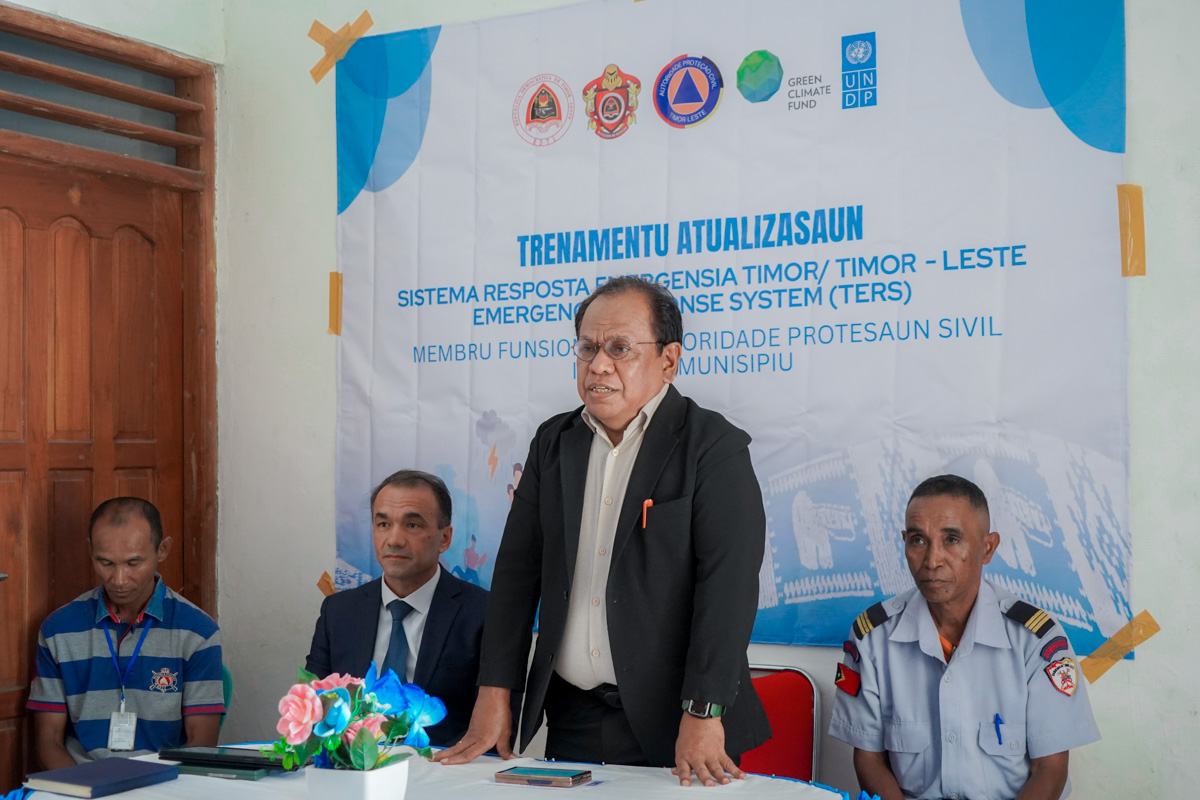 Photograph of a man in a suit giving a speech at a conference, with a banner behind.