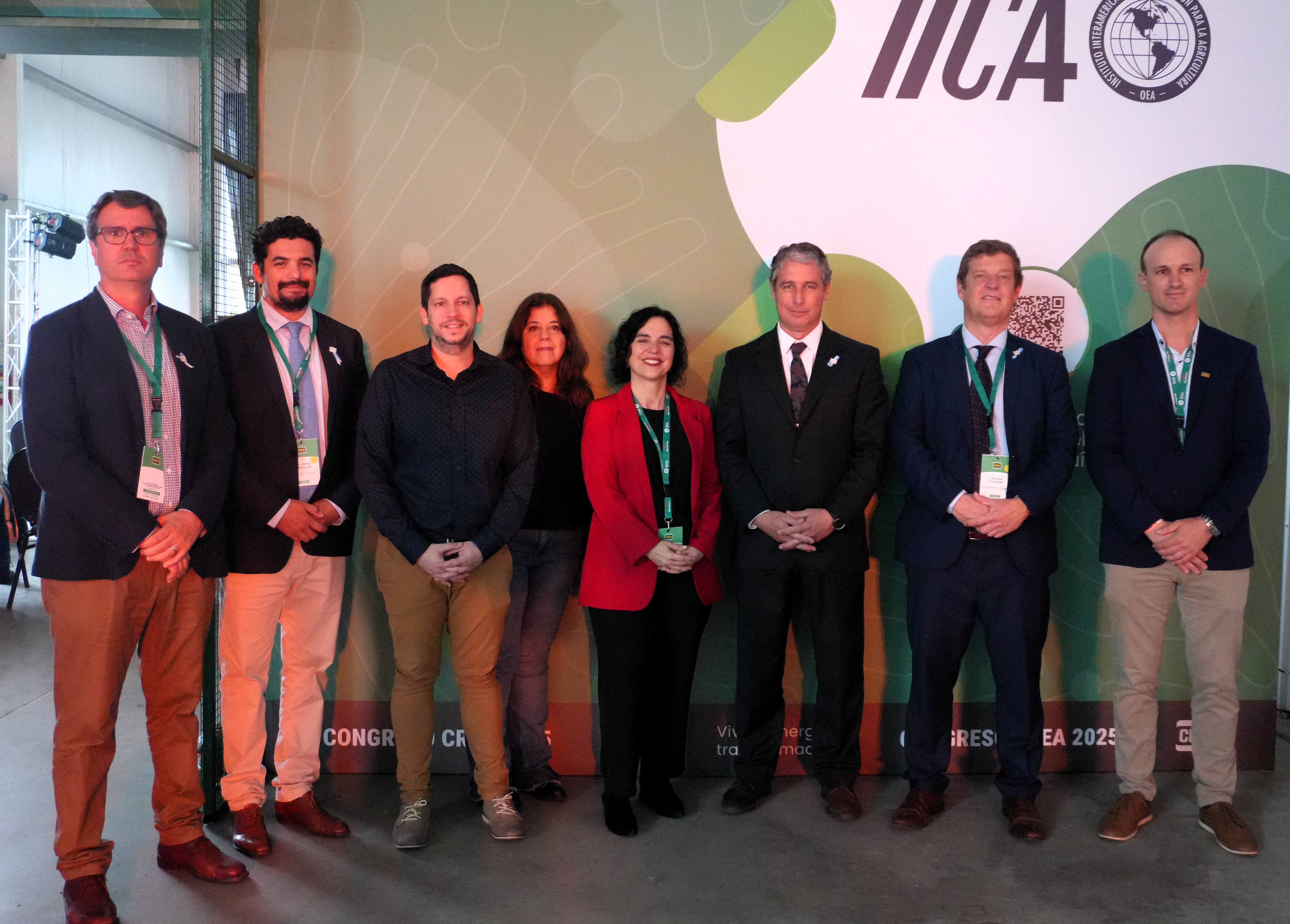 Nine professionals in business attire pose for a group photo at a conference backdrop.