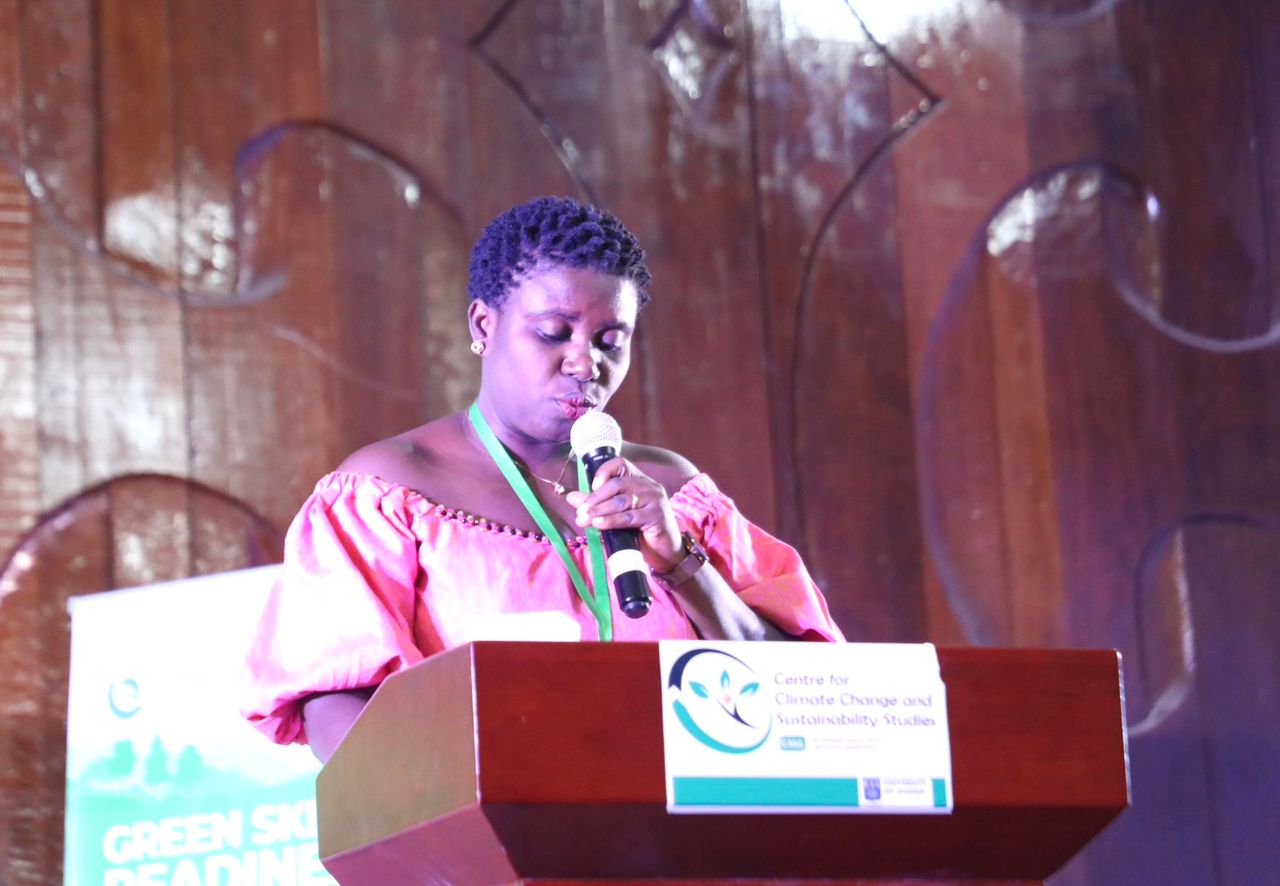 Speaker at podium delivering a presentation; pink top, wooden backdrop, banners