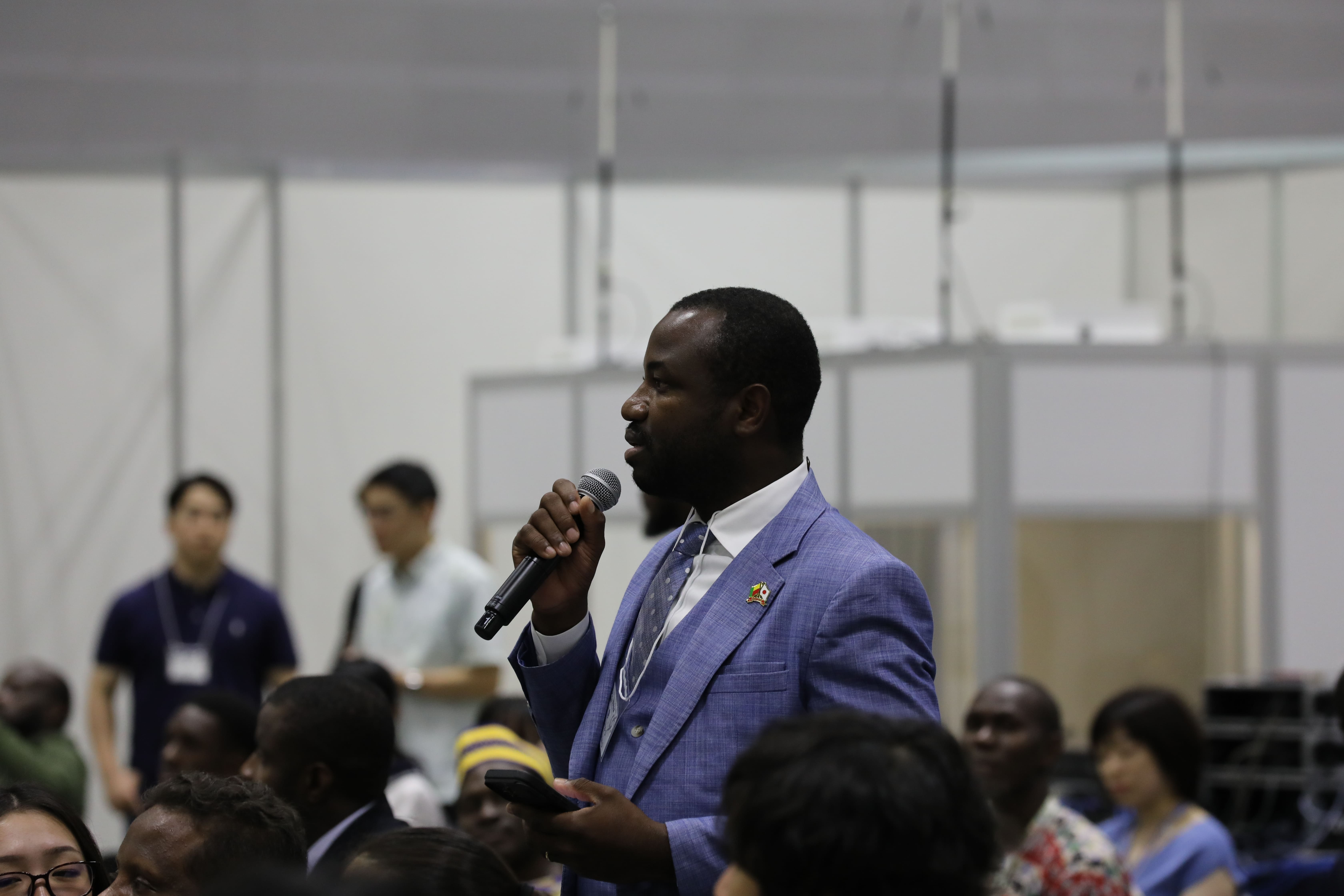 Speaker in a blue suit addresses a crowd at an indoor event.