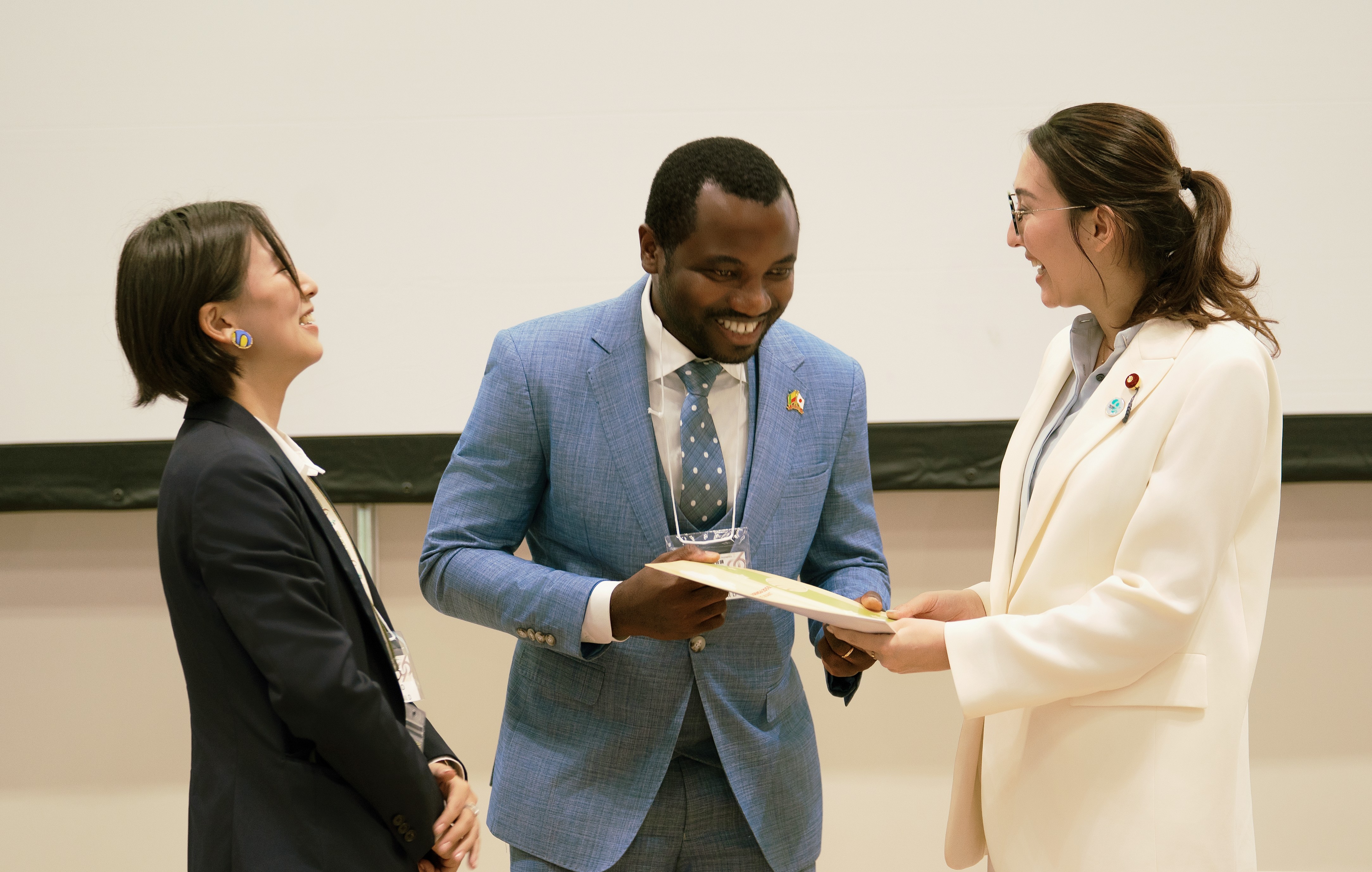Photograph of two women and a man exchanging a document in a conference room.