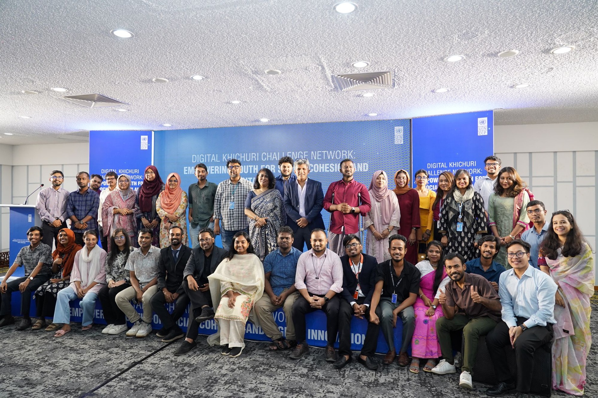 Diverse group posing for a photo in a conference room with a blue backdrop.