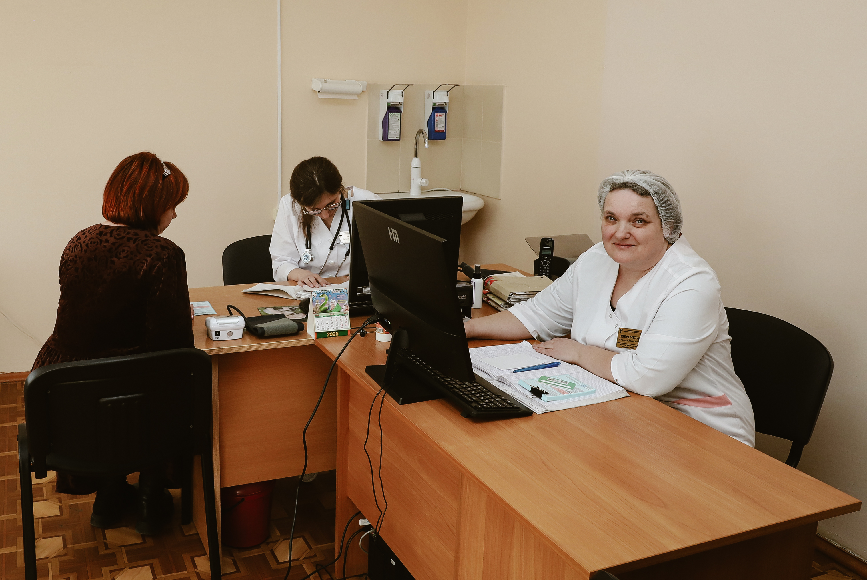 Clinic scene: patient seated opposite a smiling clinician at a desk with a computer.