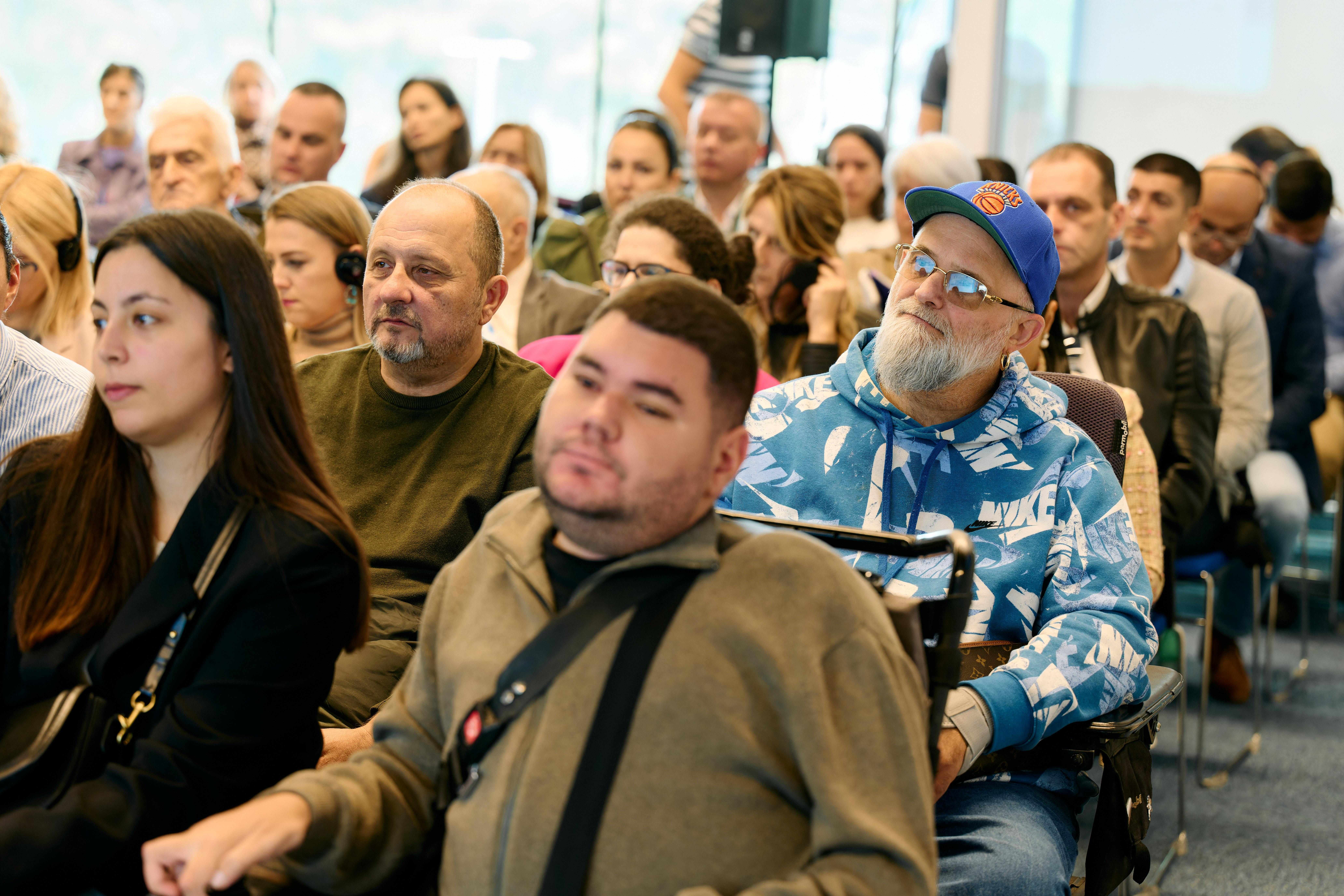 Audience seated in a conference room, diverse attendees listening to a speaker.