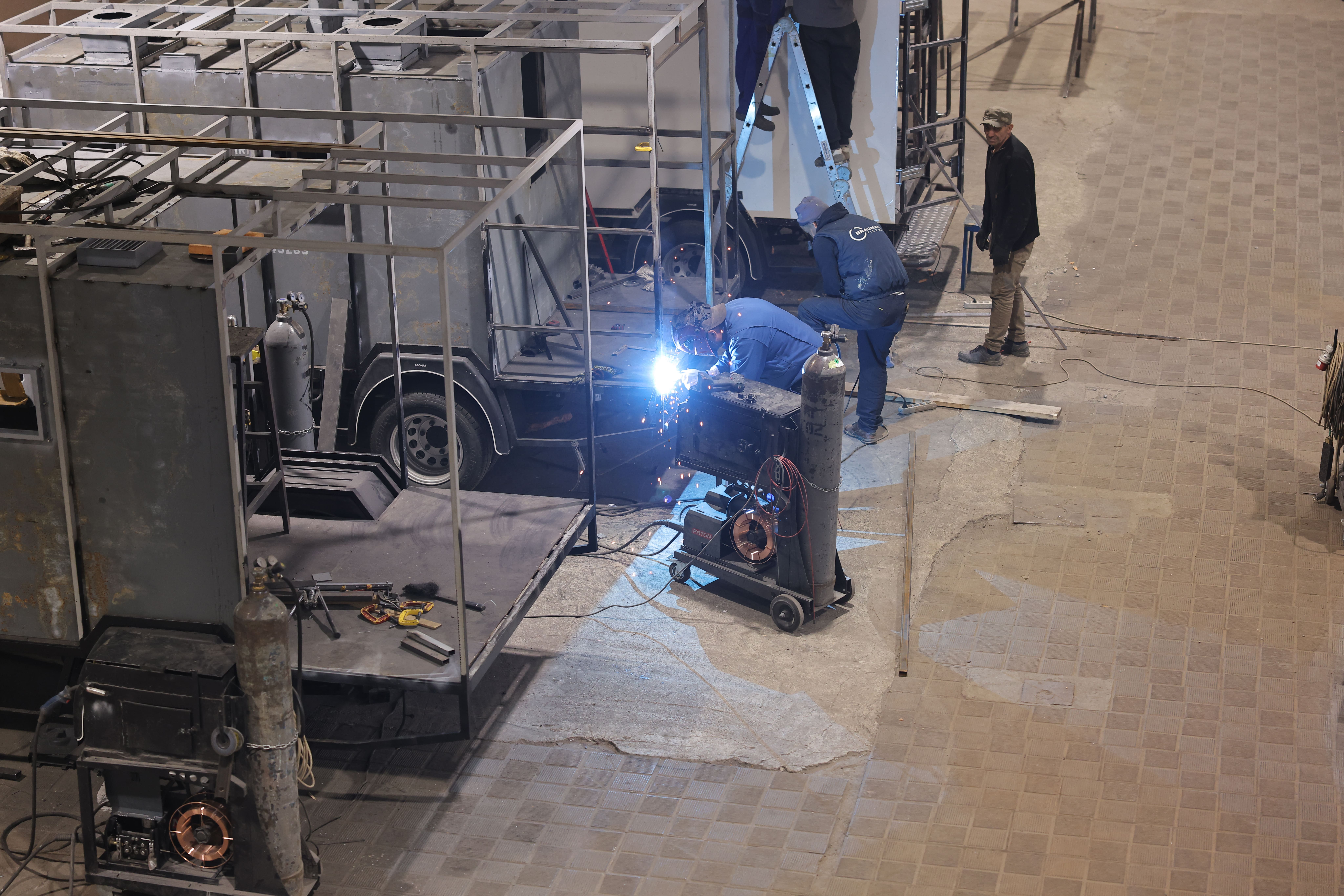 Backstage scene with metal truss, lighting rig, and a technician adjusting gear.