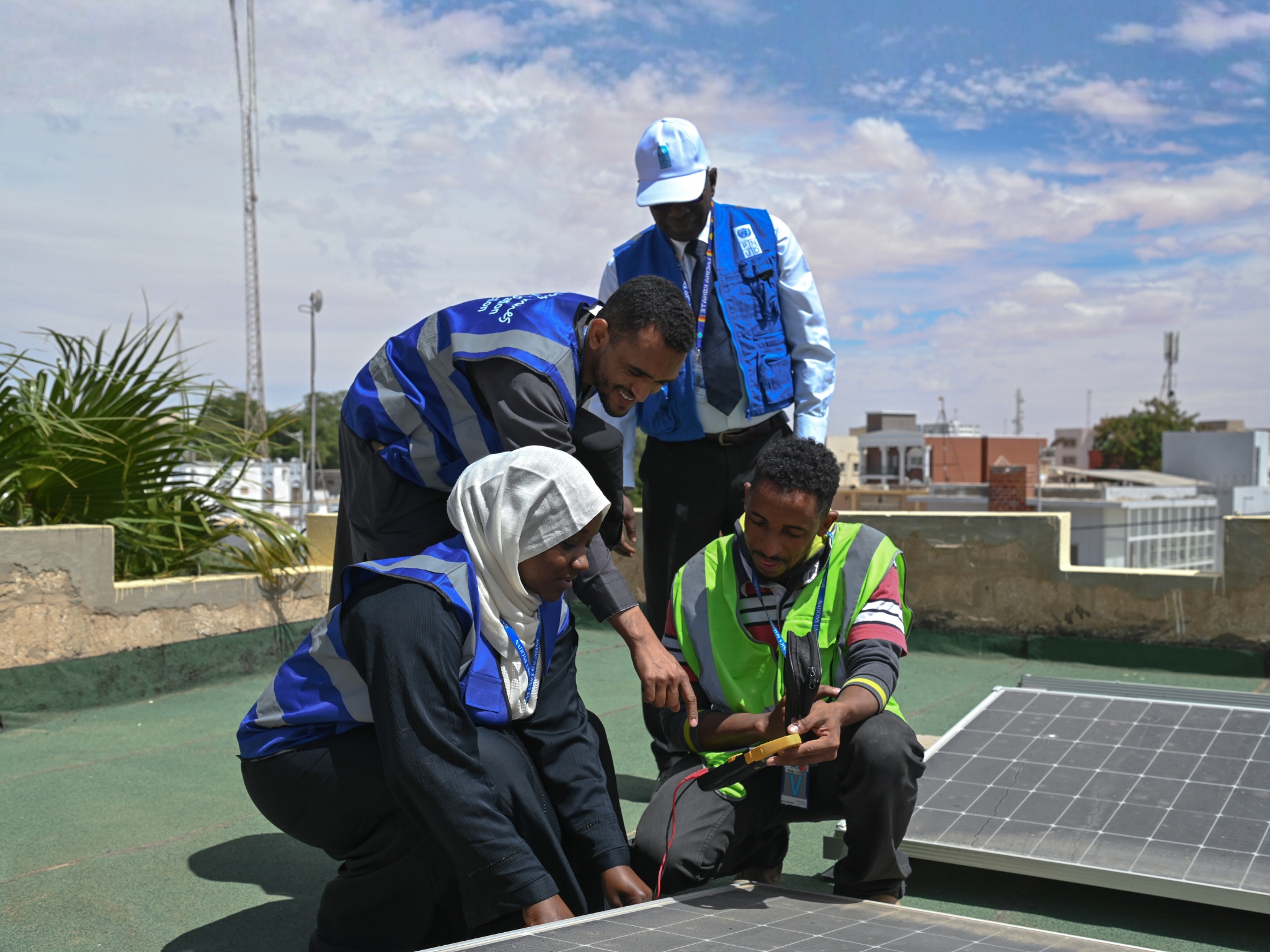 Mauritania - three people in safety vests inspecting solar panels on a rooftop.