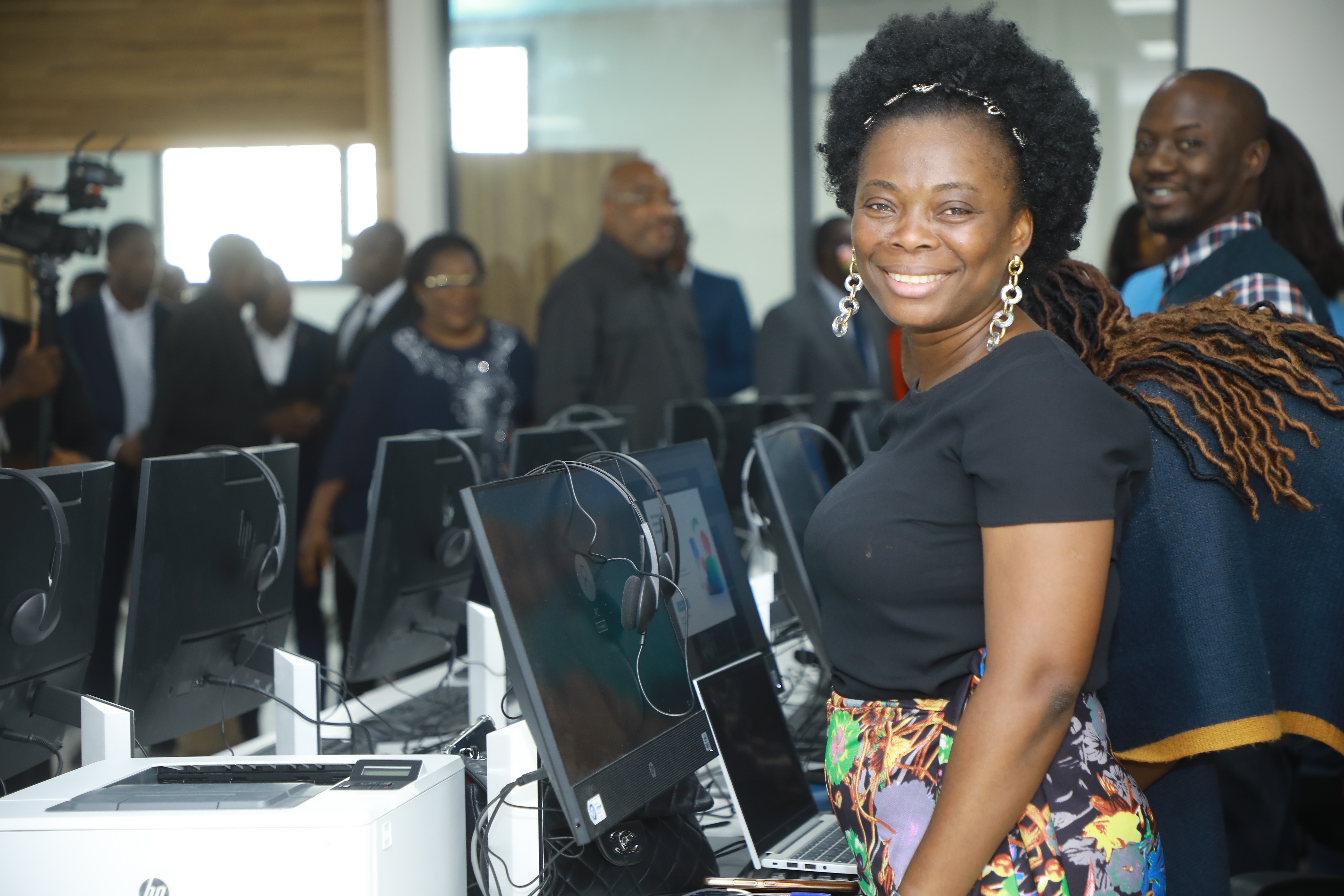 Woman with braided hair beside laptops at a tech expo; a crowd watches.