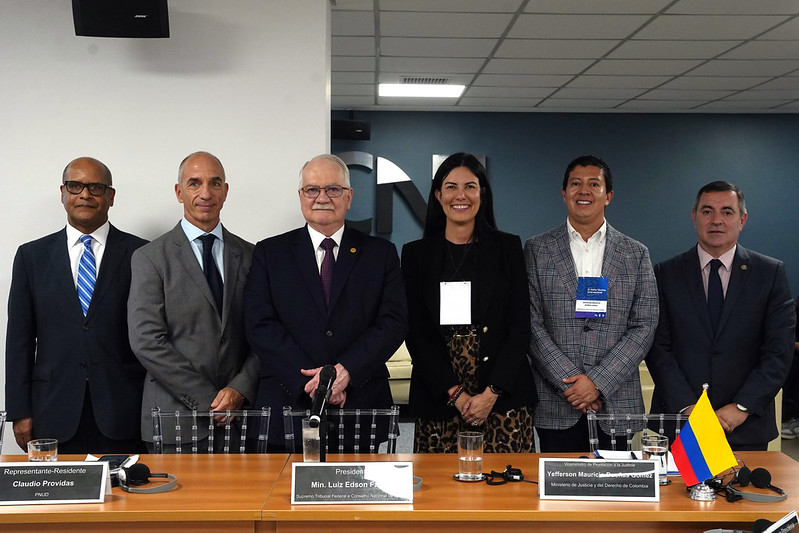 Six professionals in business attire stand behind a conference table with nameplates